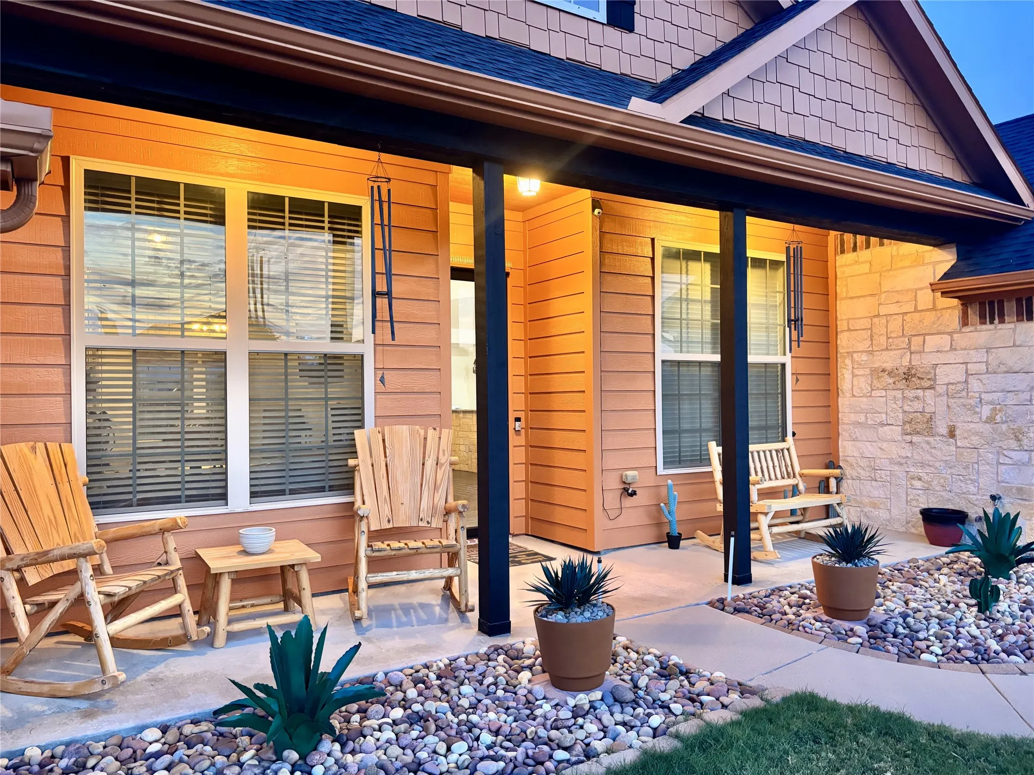Covered front porch with stone and horizontal siding exterior accents, shaker shingle gable, dark roofline, and integrated gutters