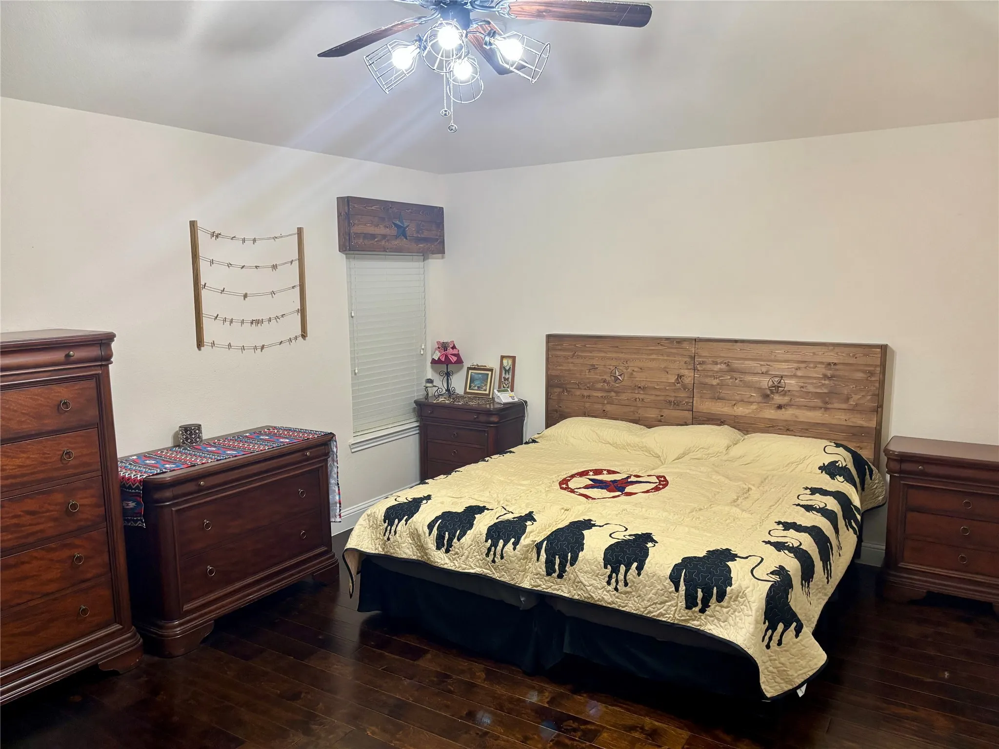 Spacious bedroom featuring a wood-finish bed frame with upholstered headboard, dark wood-finish flooring throughout, ceiling fan with integrated lighting, and ample natural light from windows