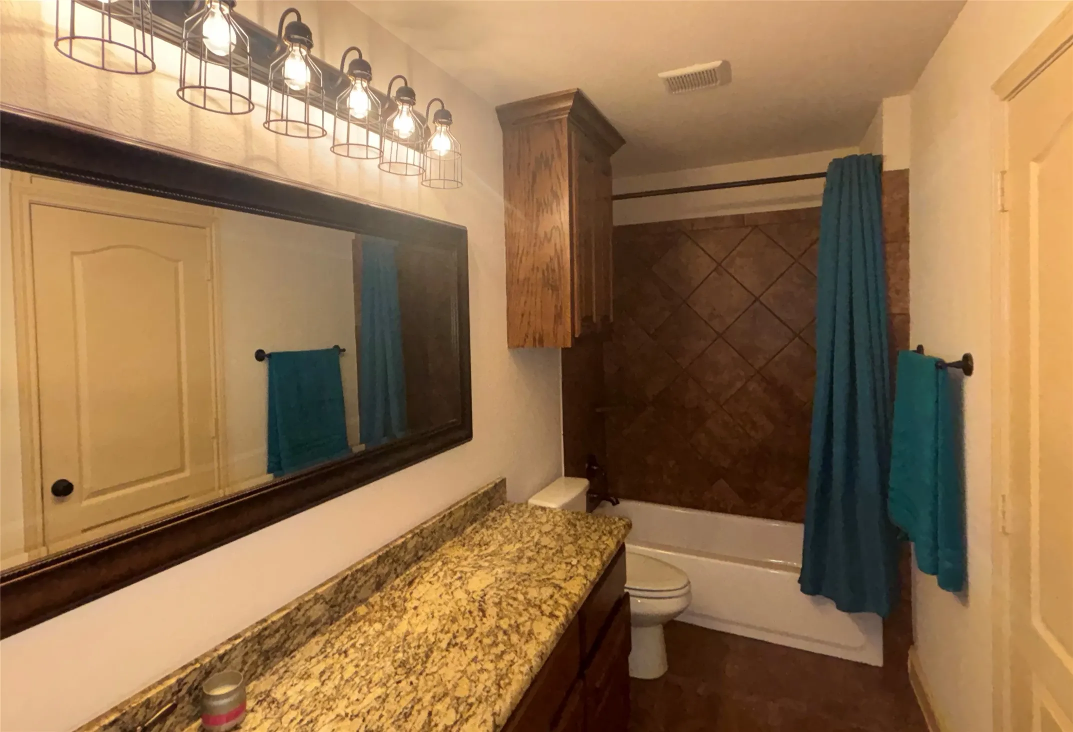 Spa-inspired bathroom featuring a granite-topped double vanity with dual sinks, an oversized framed mirror with integrated lighting, and a tiled shower surround with coordinating tile accents