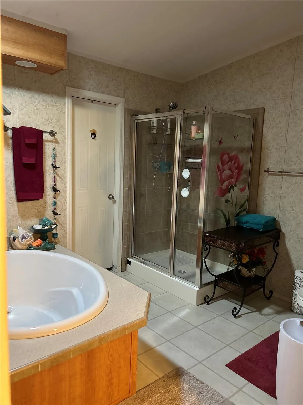 Built-in soaking tub with a light-toned countertop, glass-enclosed shower, and light-toned tile flooring