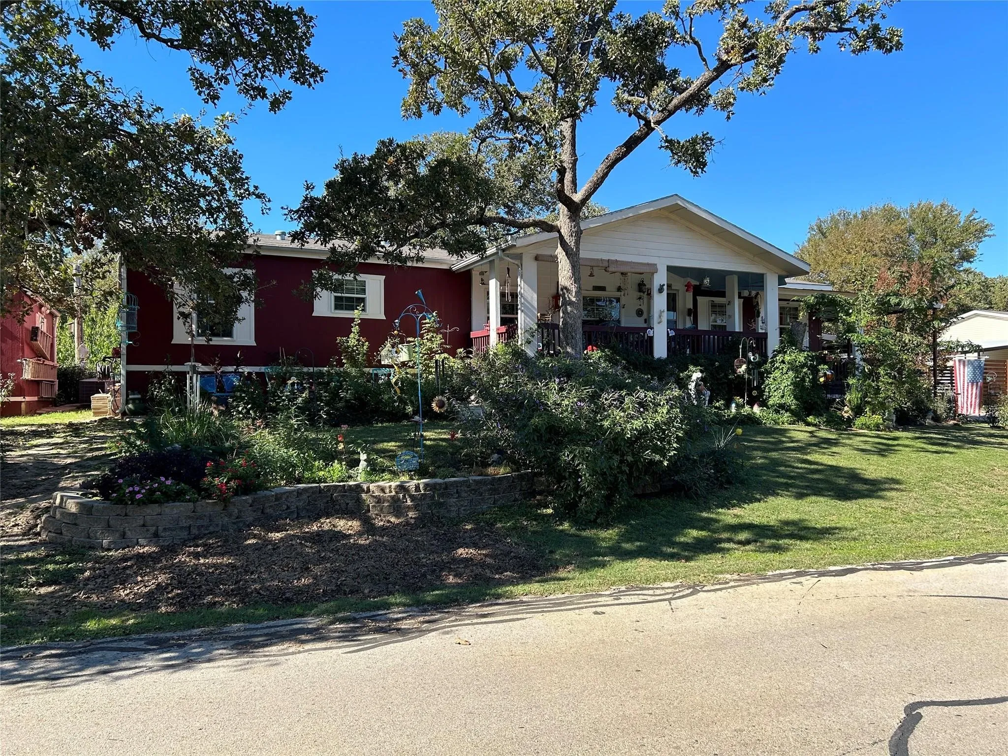 Red exterior with white trim, covered front porch, mature trees, and a tiered front yard with retaining wall