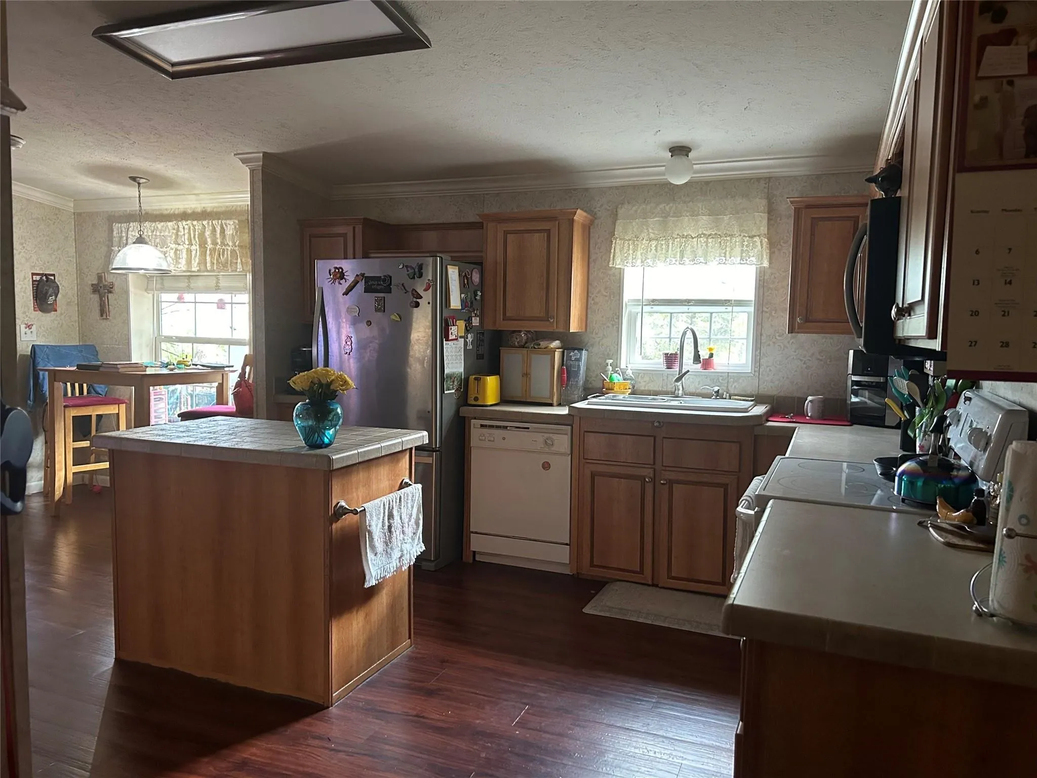 Wood-finish flooring, central island with tiled countertop, wood cabinetry, and stainless steel appliances