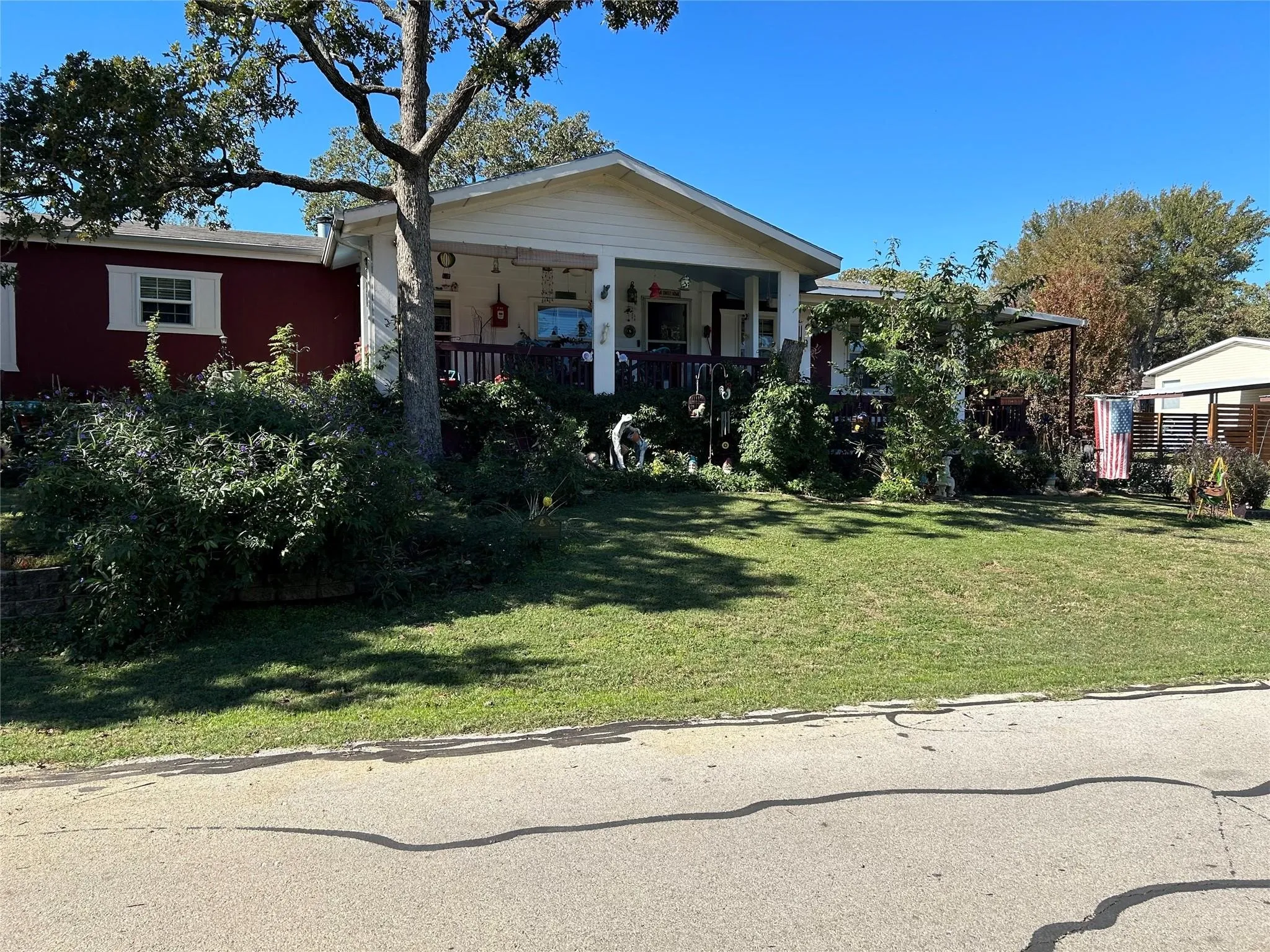 Charming cottage-style home featuring a covered front porch with classical columns, manicured front lawn with mature landscaping, and detached outbuildings