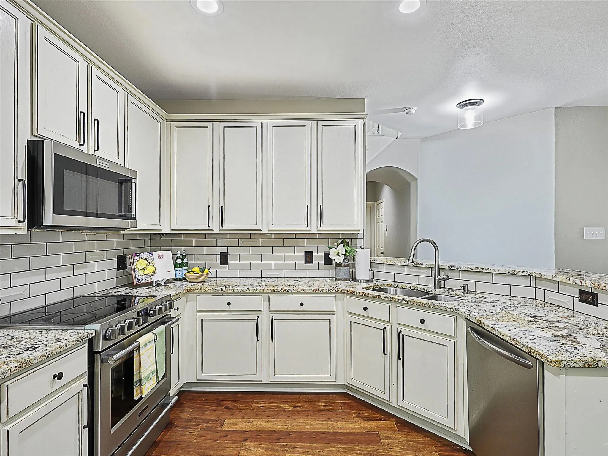 Kitchen featuring white cabinetry, stainless steel appliances, a subway tile backsplash, granite countertops, and wood-finish flooring