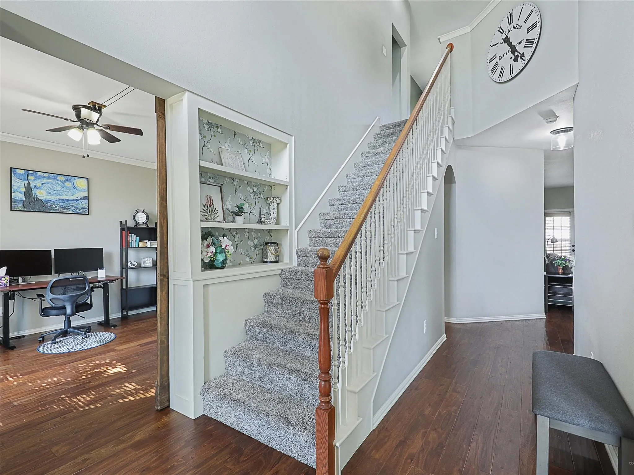 Bright foyer showcasing hardwood flooring, a curved staircase with wood handrail and white balusters, recessed lighting, and a wall-mounted clock