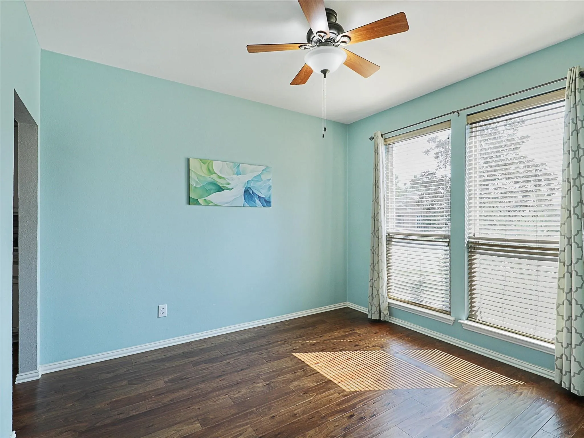 Wood-finish flooring, ceiling fan with wood-tone blades, white trim, and dual windows with blinds