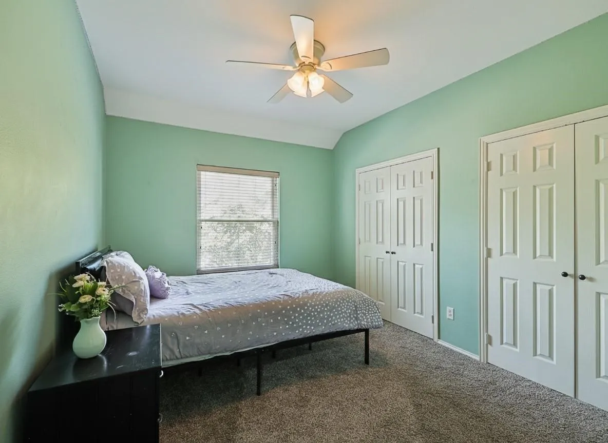 Bedroom featuring light green walls, a window with horizontal blinds, a ceiling fan with integrated lighting, and two sets of bi-fold closet doors