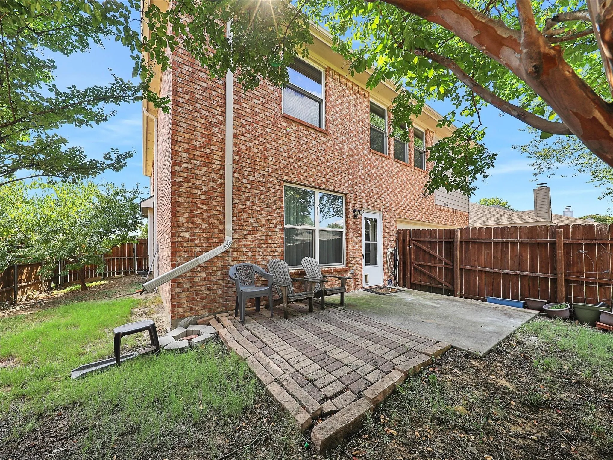 Brick exterior featuring multiple windows, a white entry door, and an integrated patio with paver and concrete sections