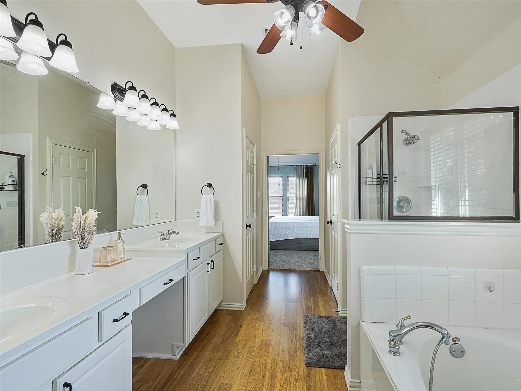 Spa-inspired primary bathroom featuring dual vanities with white cabinetry, quartz countertops, and chrome fixtures