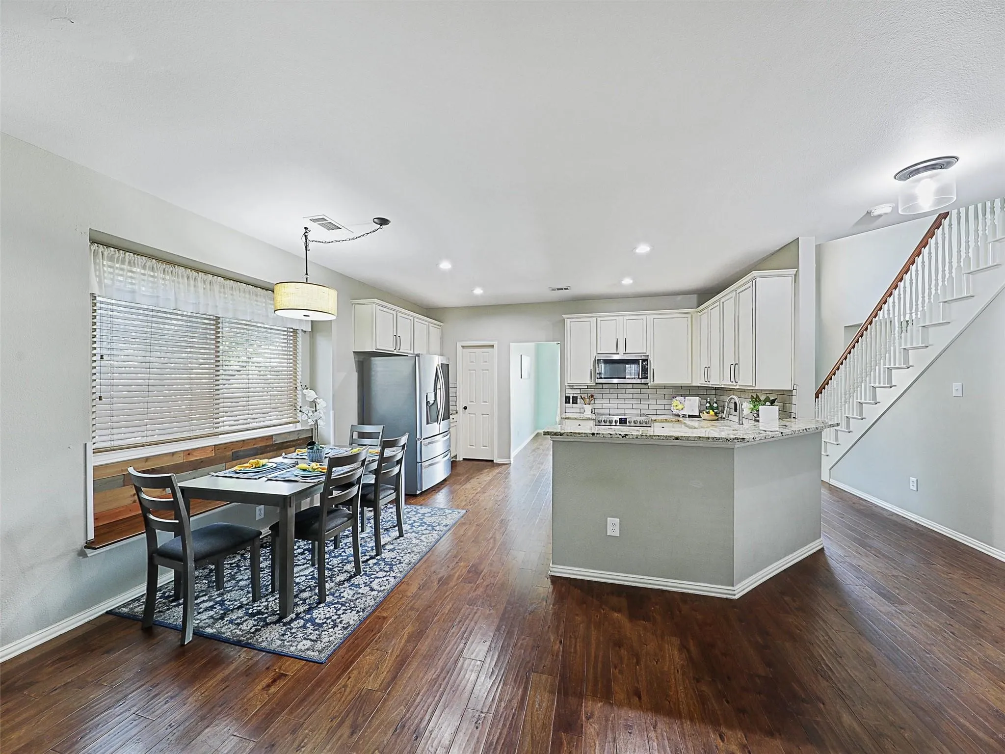 Open-concept kitchen and dining area featuring stainless steel appliances, granite countertops, a center island with pendant lighting, and wood-finish flooring throughout