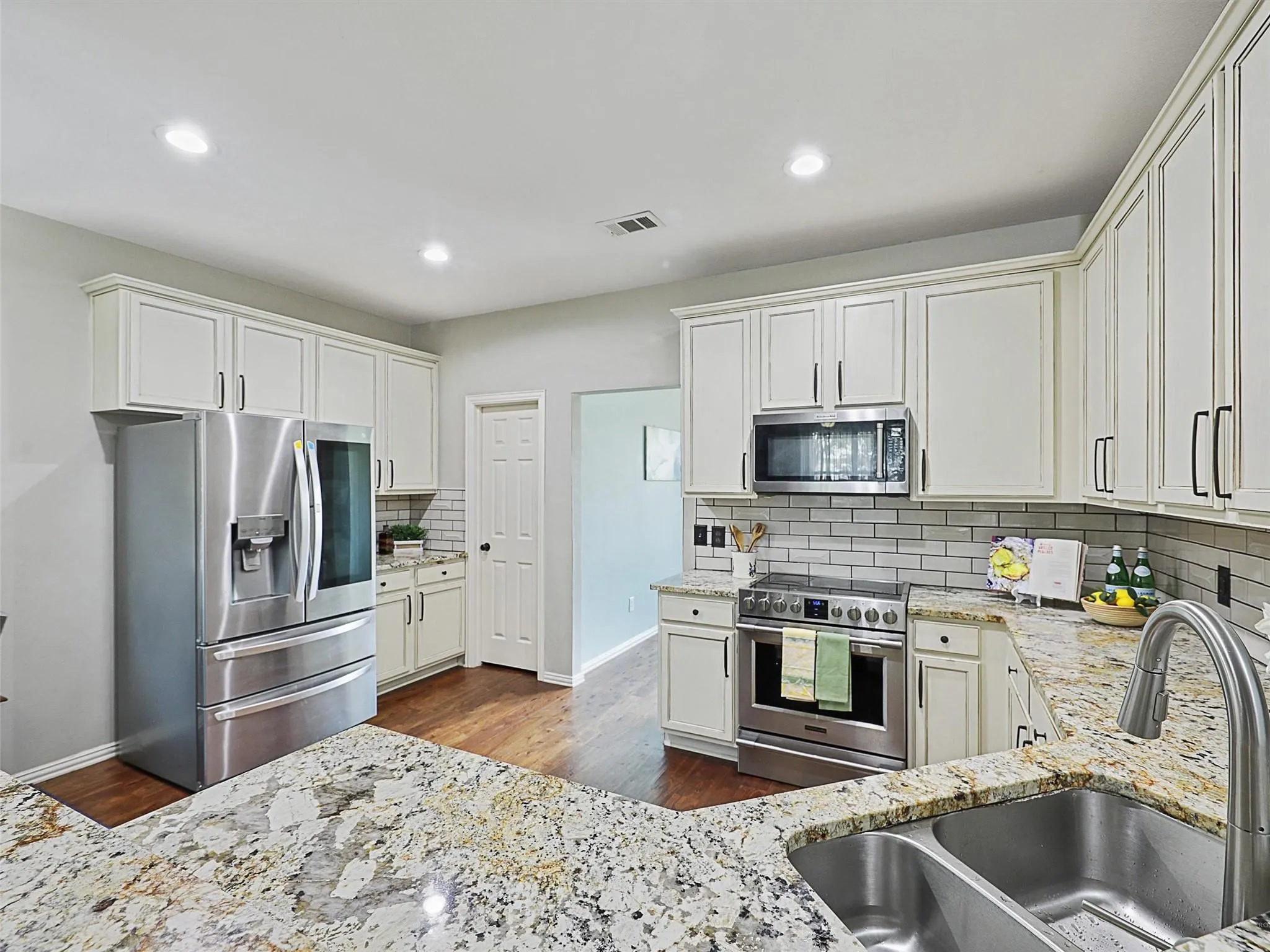 Gourmet kitchen featuring crisp white cabinetry with brushed nickel hardware, quartz countertops with subtle veining, stainless steel appliances including a French-door refrigerator and built-in microwave, subway tile backsplash, and an undermount sink with pull-down faucet