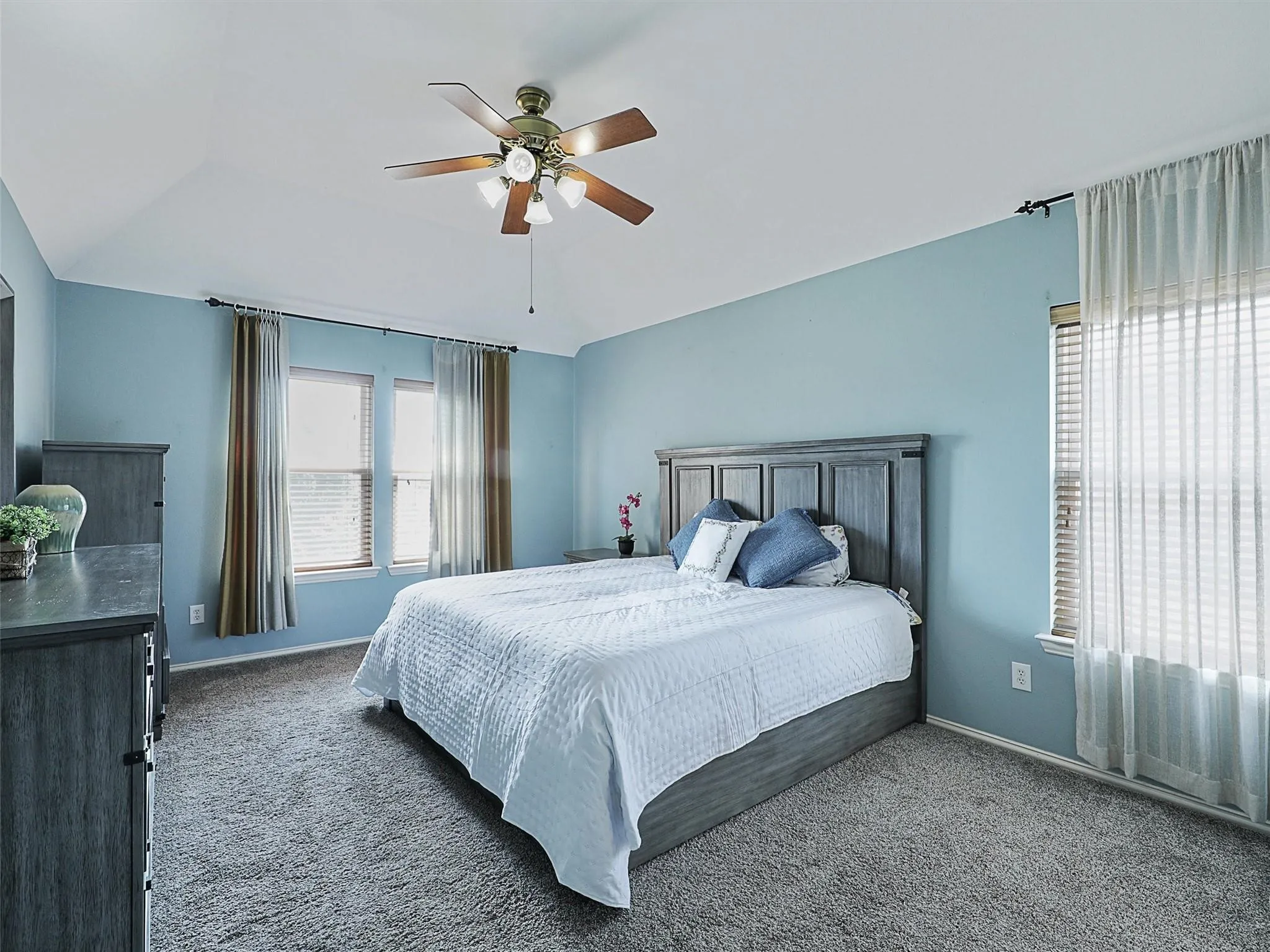 Vaulted ceiling with an attached ceiling fan, carpet flooring, and window treatments