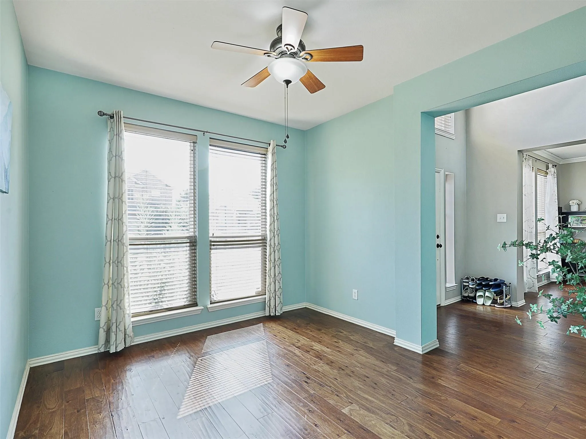 Wood-finish flooring throughout, two large windows with blinds, and a ceiling fan with light fixture