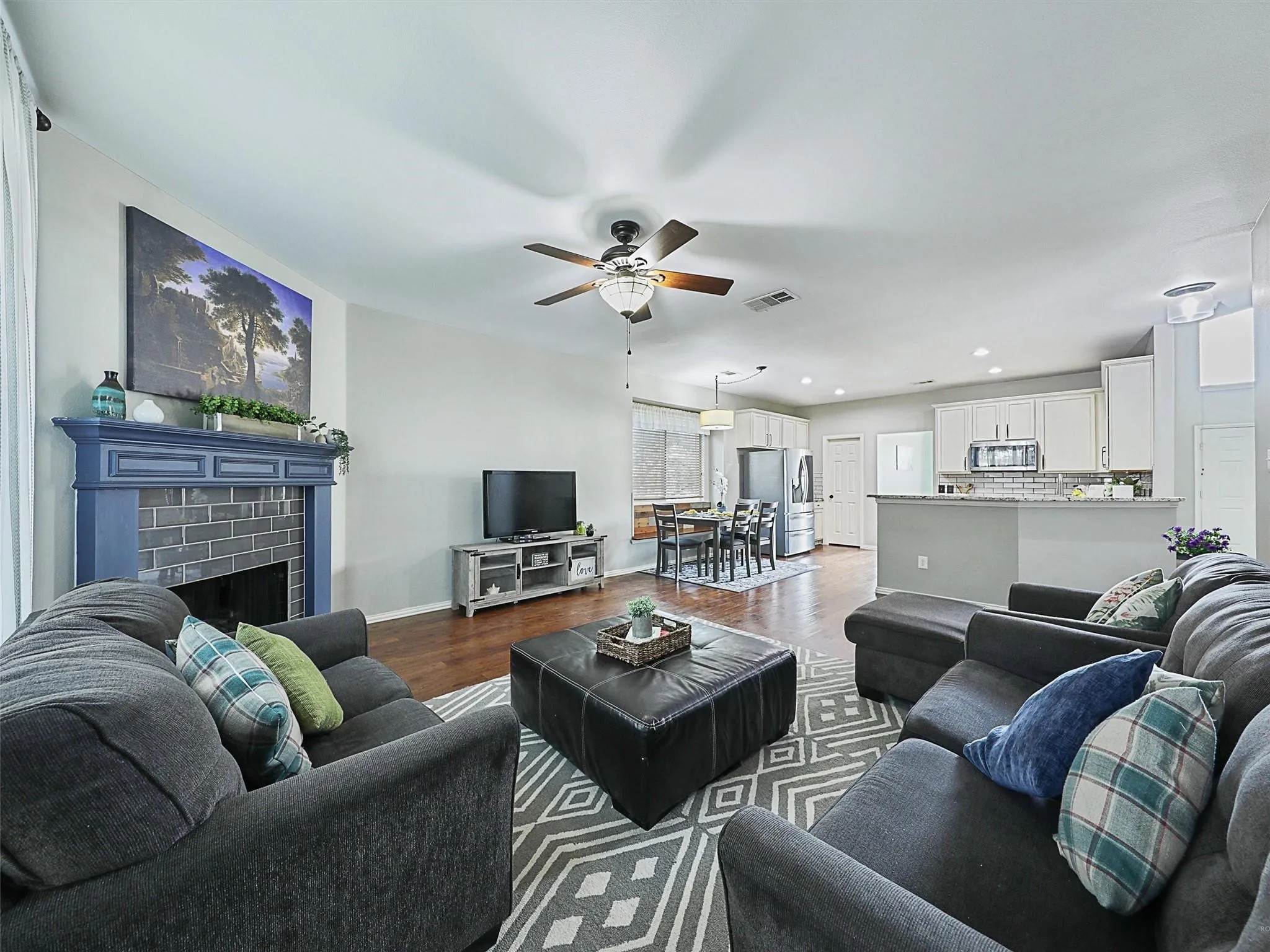 Open-concept living area featuring hardwood flooring, a ceiling fan with integrated lighting, and a fireplace with blue-tiled surround