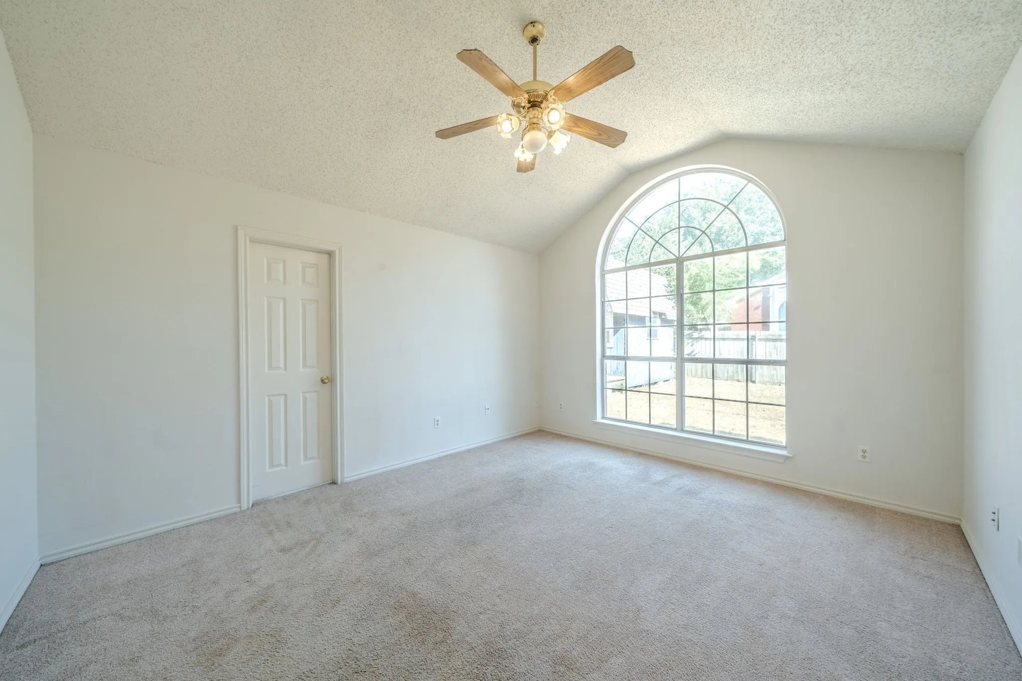 Large primary bedroom with vaulted ceiling, a beautiful oversized arched window, and ceiling fan. Lots of room here!