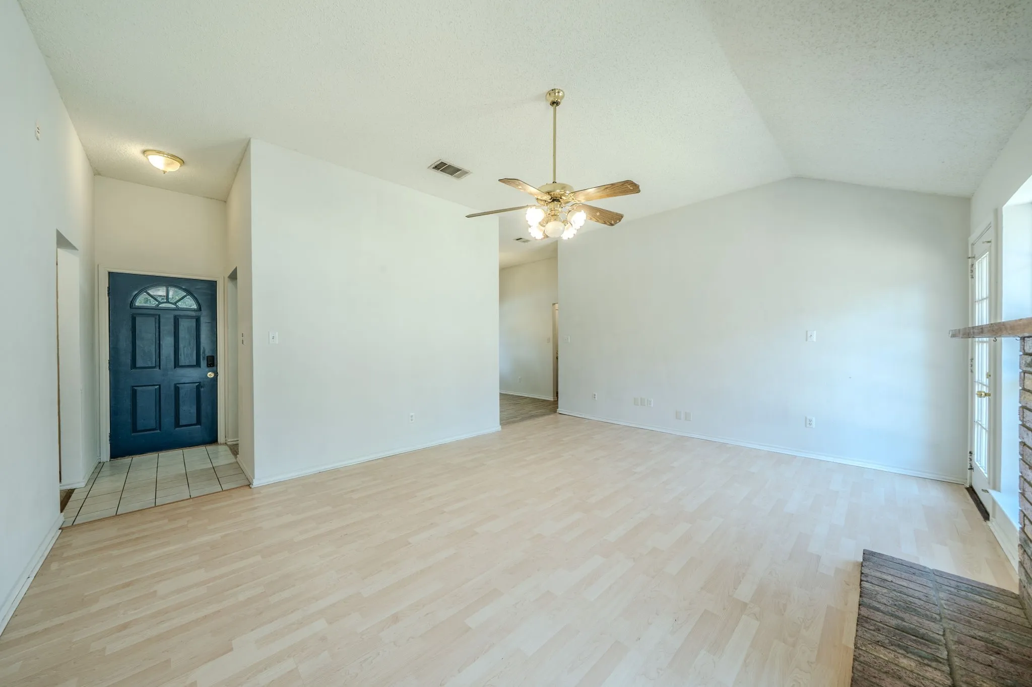 Spacious living room featuring a vaulted ceiling, wood-burning fireplace, ceiling fan, and abundant natural light.