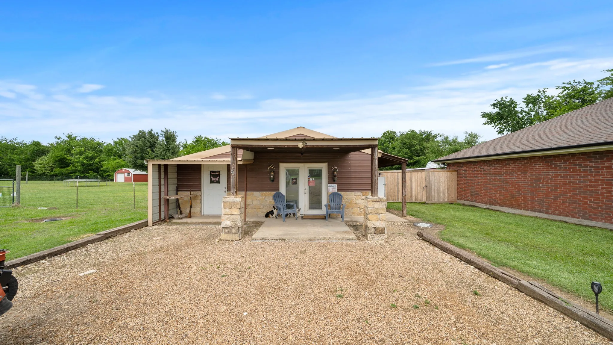 workshop or office Spacious covered patio with stone pillars and wood-finish ceiling, opening onto expansive grounds featuring manicured lawn, mature trees, and perimeter fencing