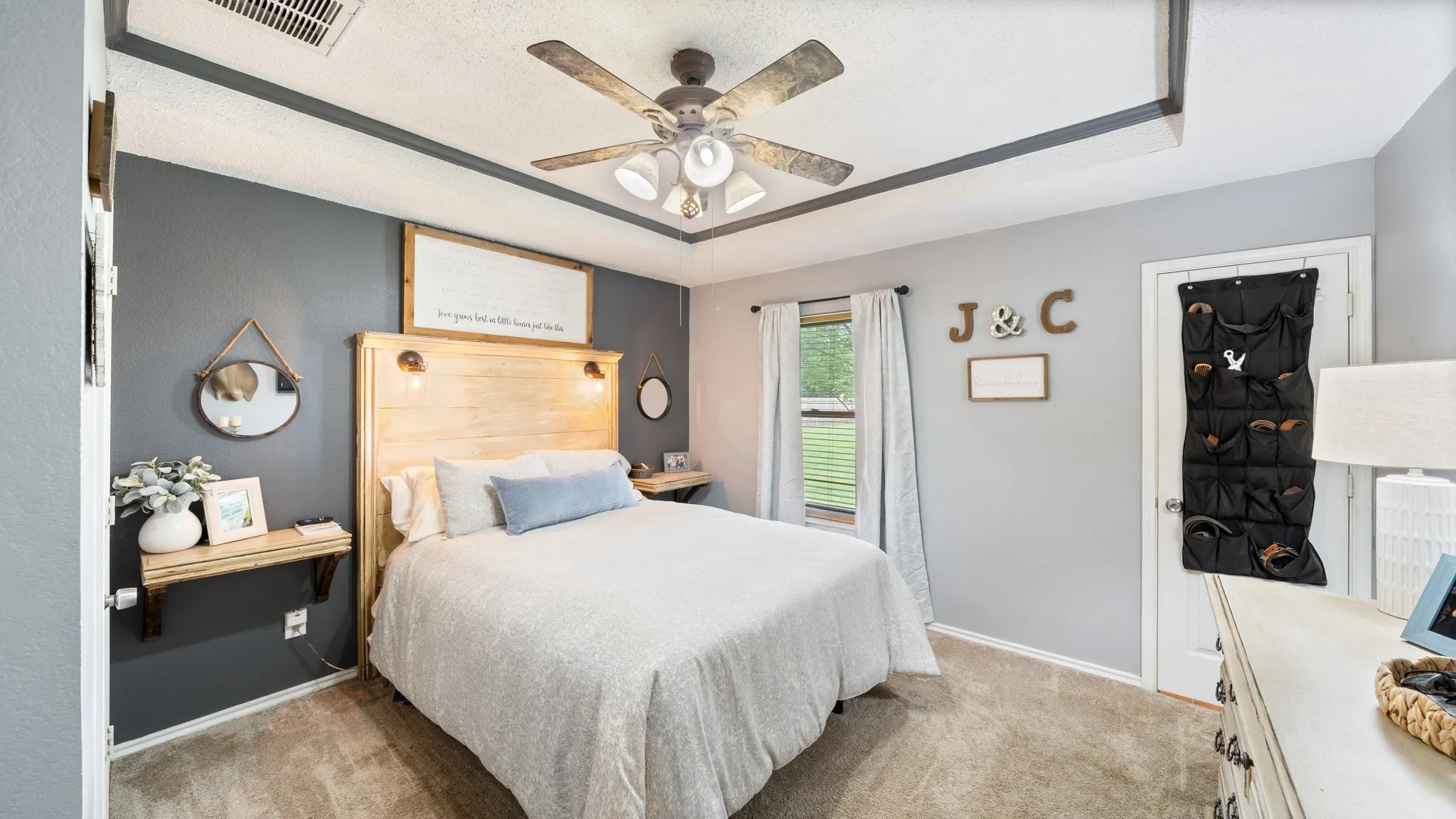 Bright, light-filled bedroom featuring a wood-finish headboard with integrated nightstands, neutral wall-to-wall carpeting, and dual-tone painted walls with crisp white trim