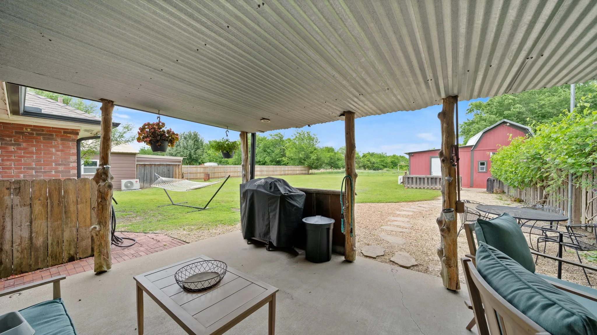 Expansive covered patio with corrugated metal roof supported by wooden posts, concrete flooring, and direct access to manicured lawn