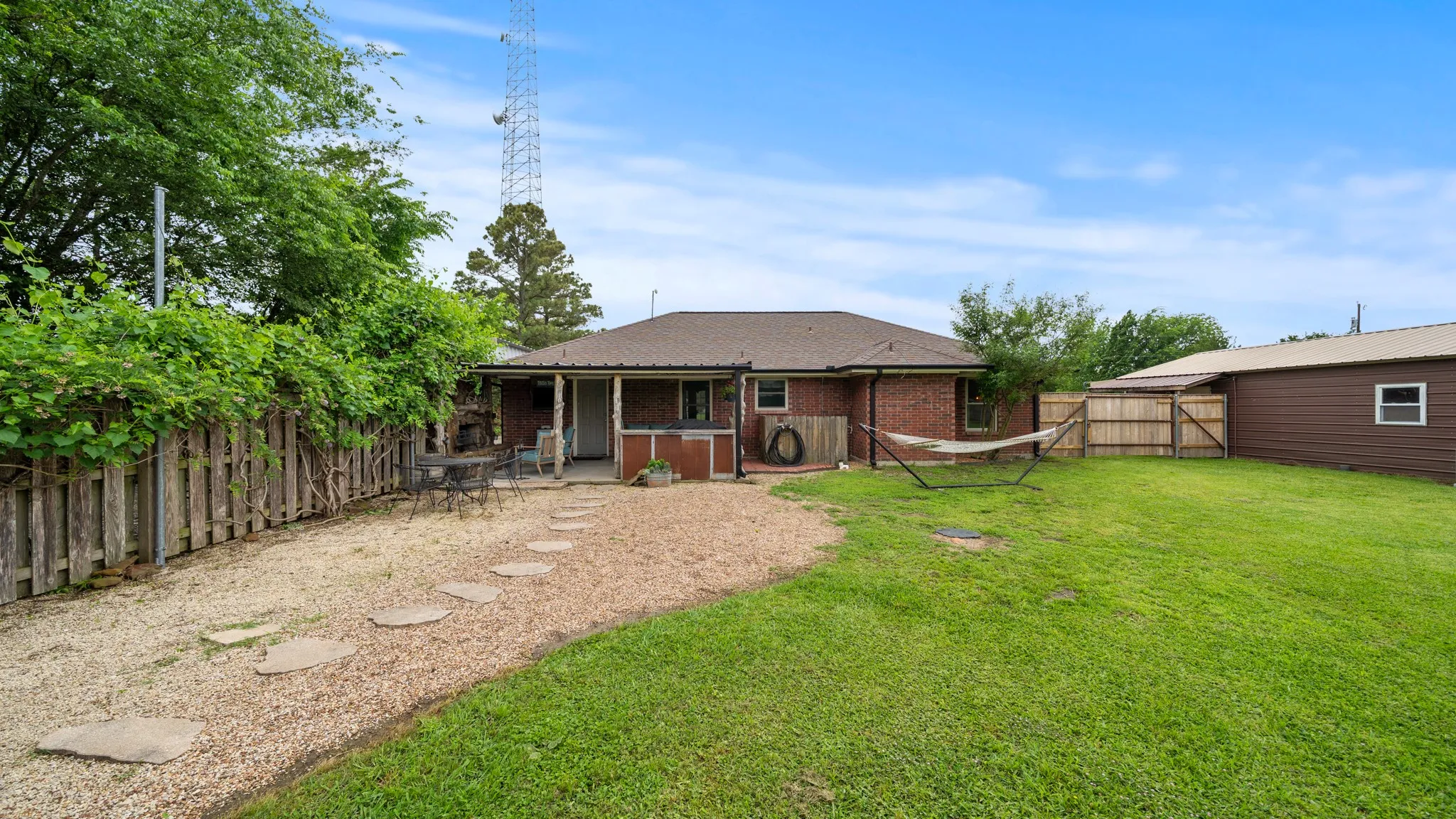Expansive grounds featuring mature landscaping and lush lawn, brick ranch-style home with covered front porch, detached outbuildings, and fencing defining the property perimeter