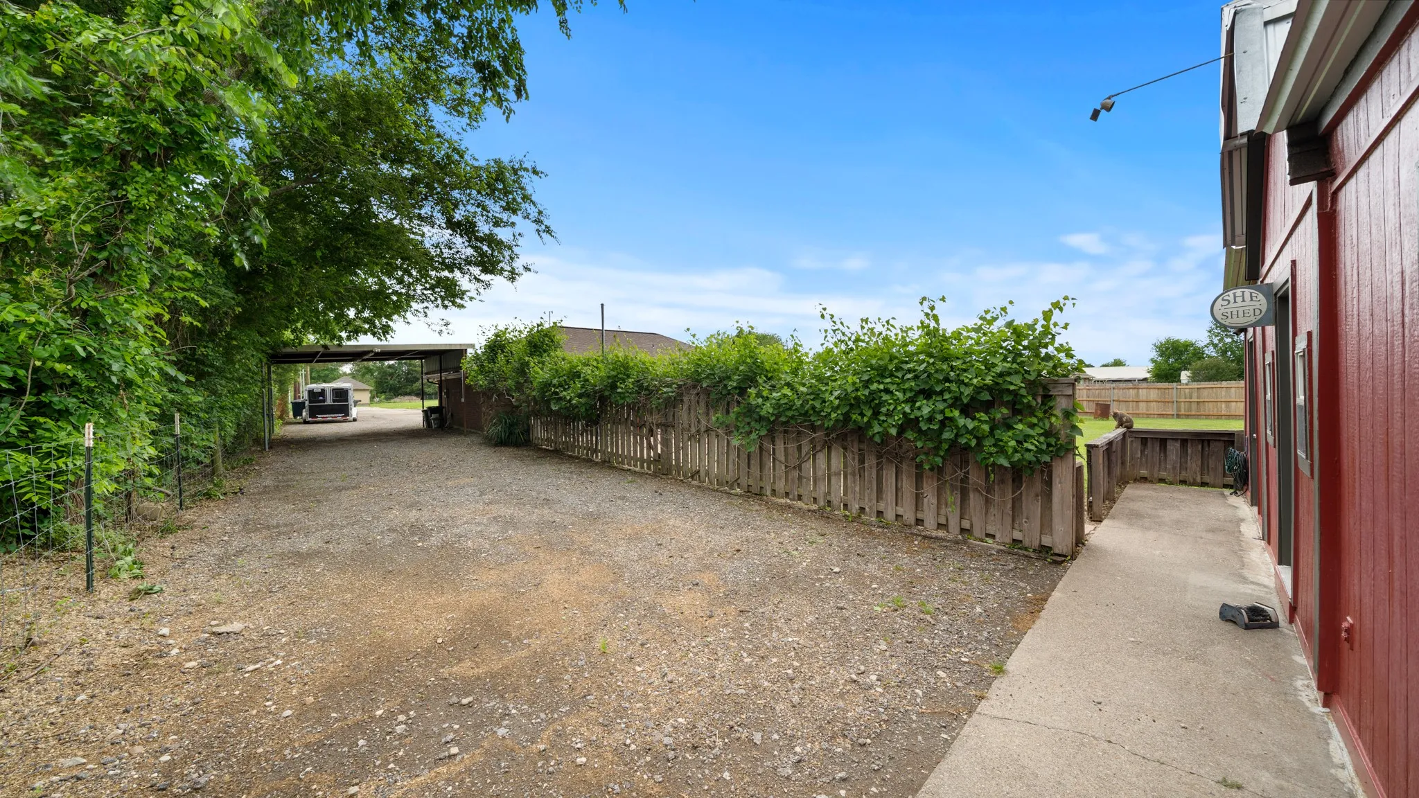 Spacious gravel courtyard with mature tree canopy, wooden perimeter fencing, and concrete pathway