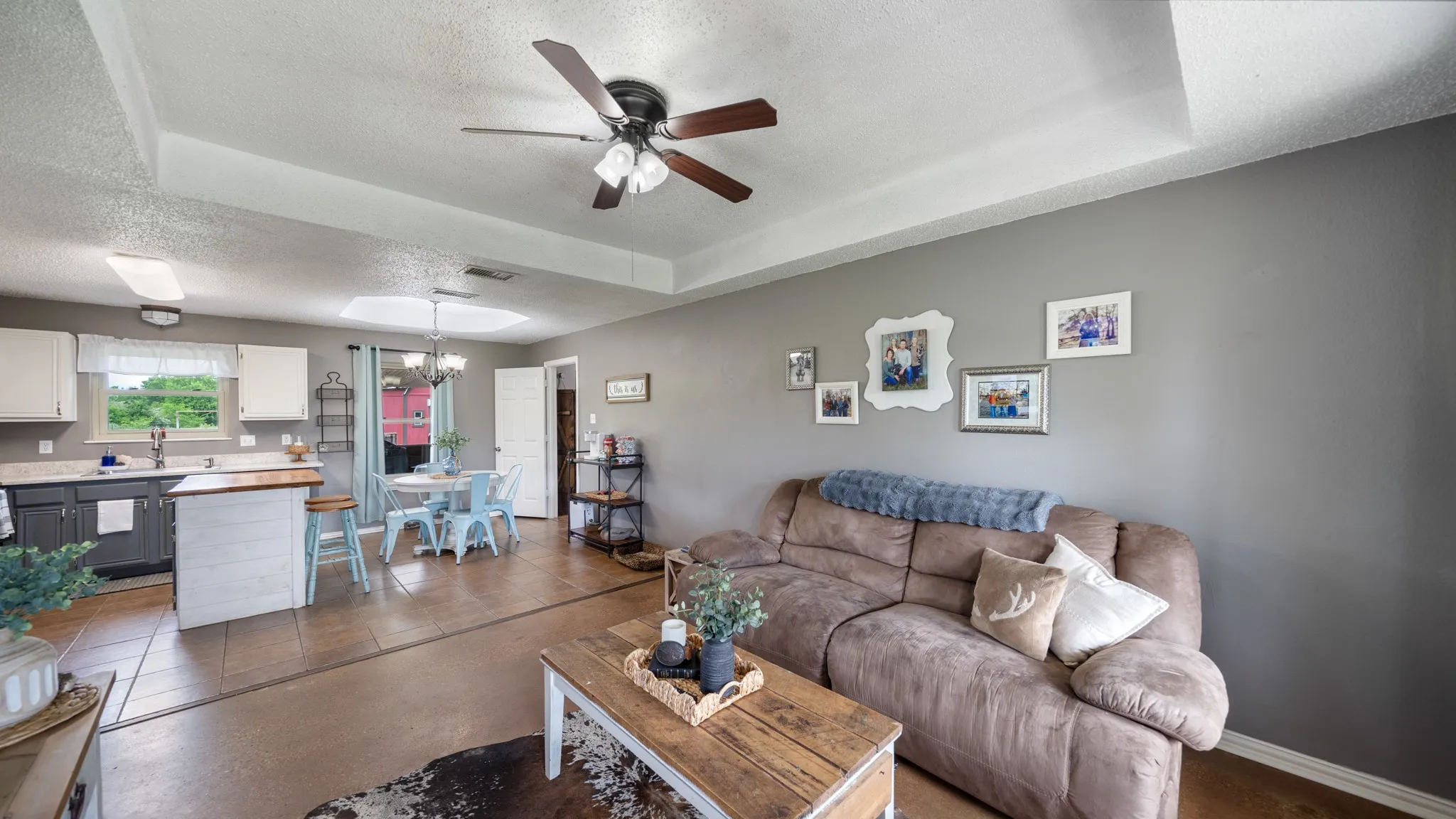 Open-concept living and kitchen area featuring wood-finish flooring throughout, a ceiling fan with integrated lighting, recessed ceiling lights, and gray painted walls