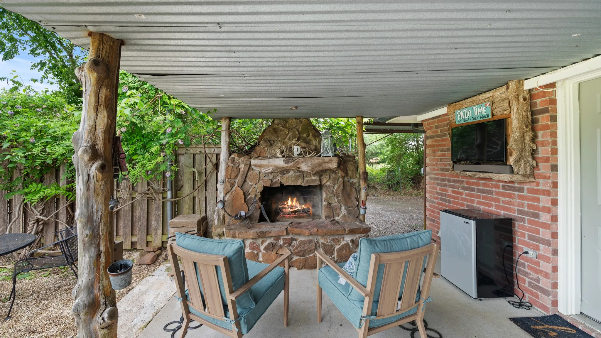 HIGHLIGHT Covered back patio with rustic stone fireplace, mature timber support posts, and metal roof