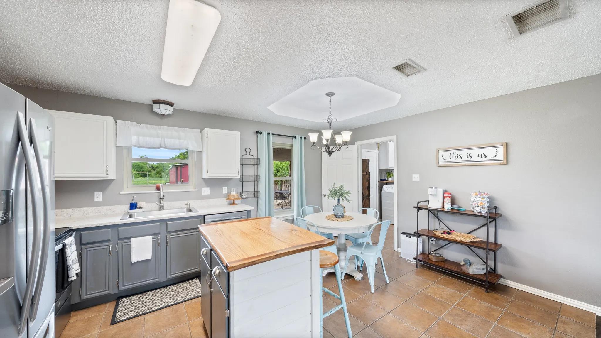 Modern kitchen featuring a two-tone cabinetry design with white upper cabinets and charcoal lower cabinets, stainless steel appliances, wood-finish island with seating, and wood-finish flooring throughout the open-concept space