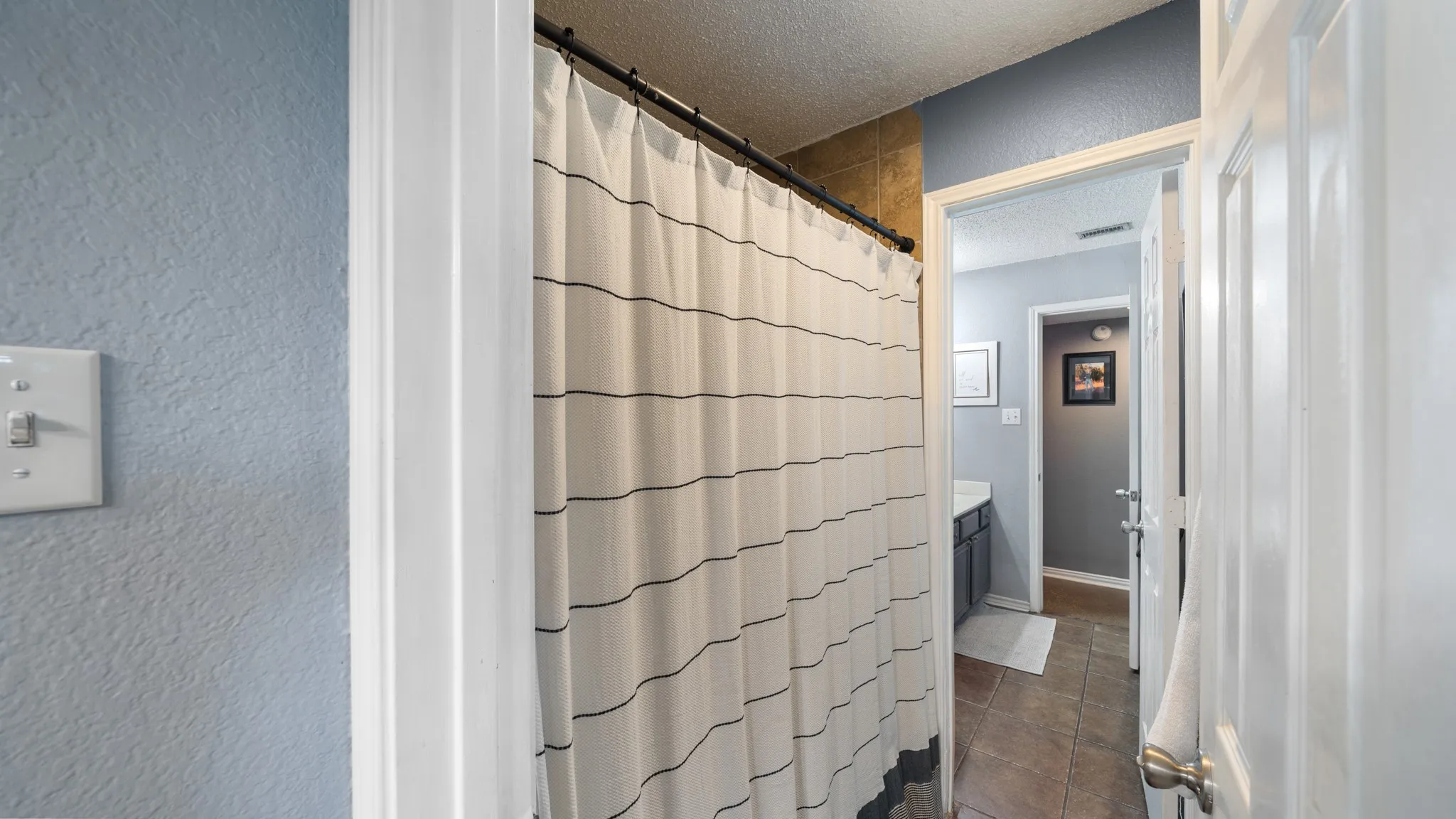 Primary bathroom featuring a tile shower enclosure with linear tile detailing, brushed metal shower rod, neutral tile surround, and ceramic flooring