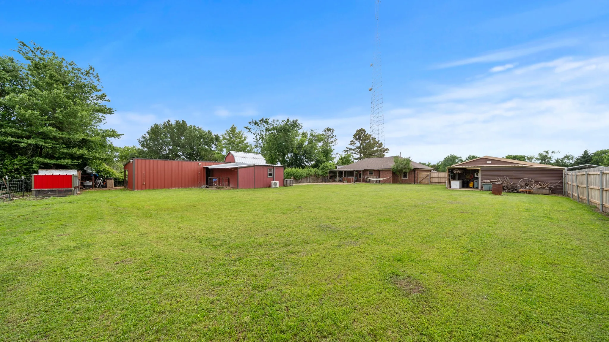 Expansive grounds featuring a manicured lawn with mature tree coverage, multiple outbuildings including red metal storage structures, and functional agricultural infrastructure with fencing throughout the property