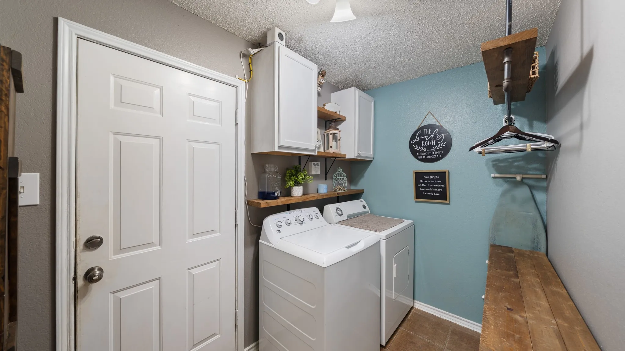 Laundry area featuring white cabinetry, wood-finish shelving, and tiled flooring