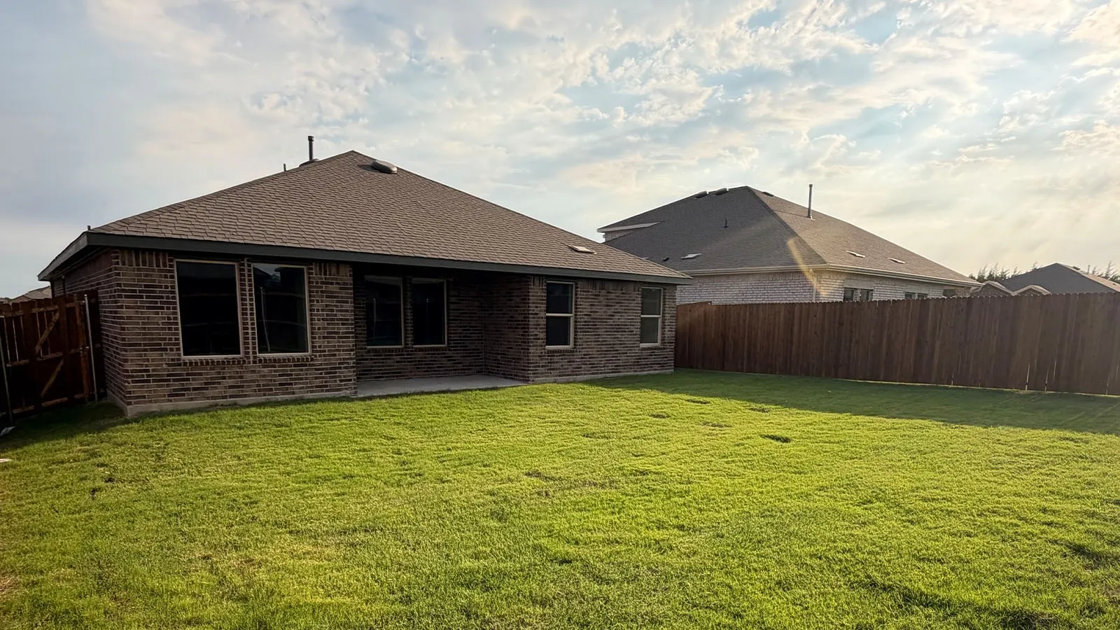 Expansive grass lawn with a wood privacy fence, brick exterior, and a concrete patio