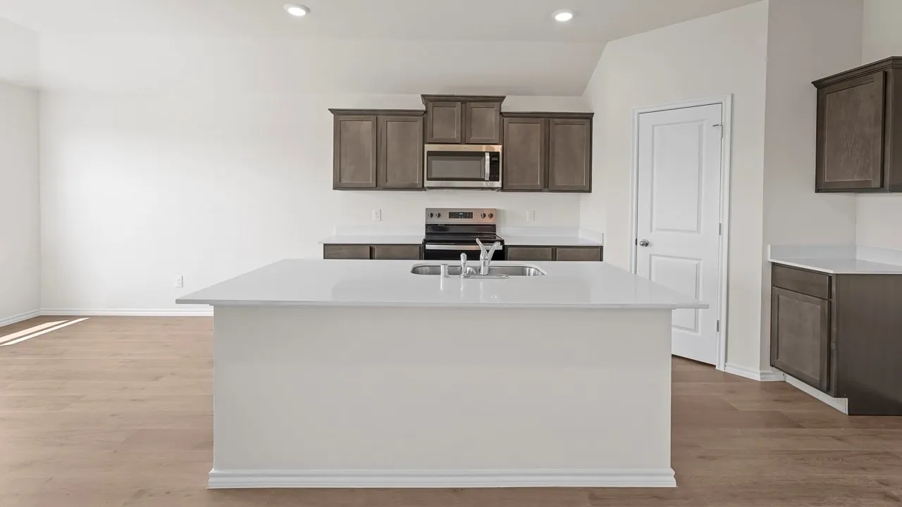 Modern kitchen featuring a large waterfall-edge island with pendant lighting, wood-finish flooring throughout, stainless steel appliances, ample cabinetry with wood-finish finishes, and quartz countertops