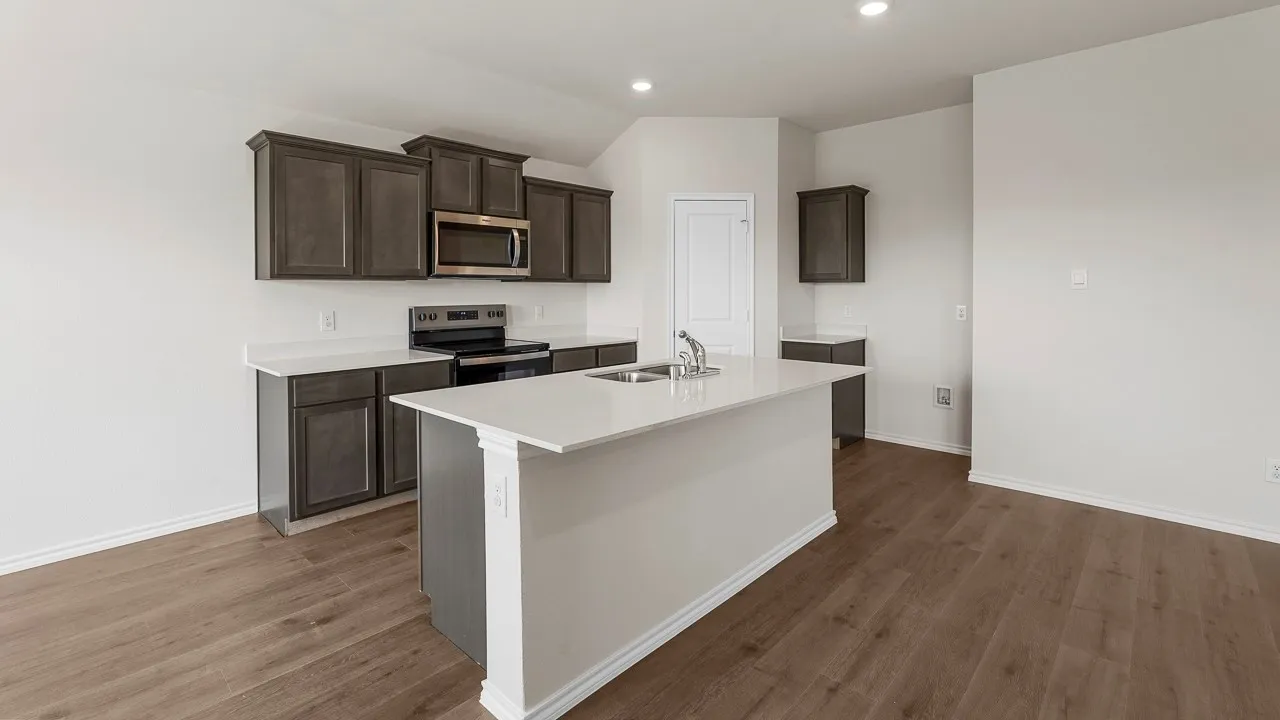 Modern kitchen featuring dark cabinetry with stainless steel appliances, white quartz countertops, a spacious center island with waterfall edge, recessed lighting, and warm wood-finish flooring throughout the open-concept living space
