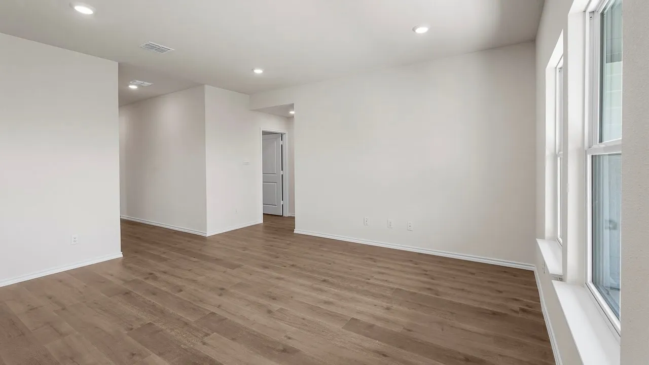 Bright, open living space featuring warm wood-finish flooring throughout, clean white walls, and abundant natural light from large windows