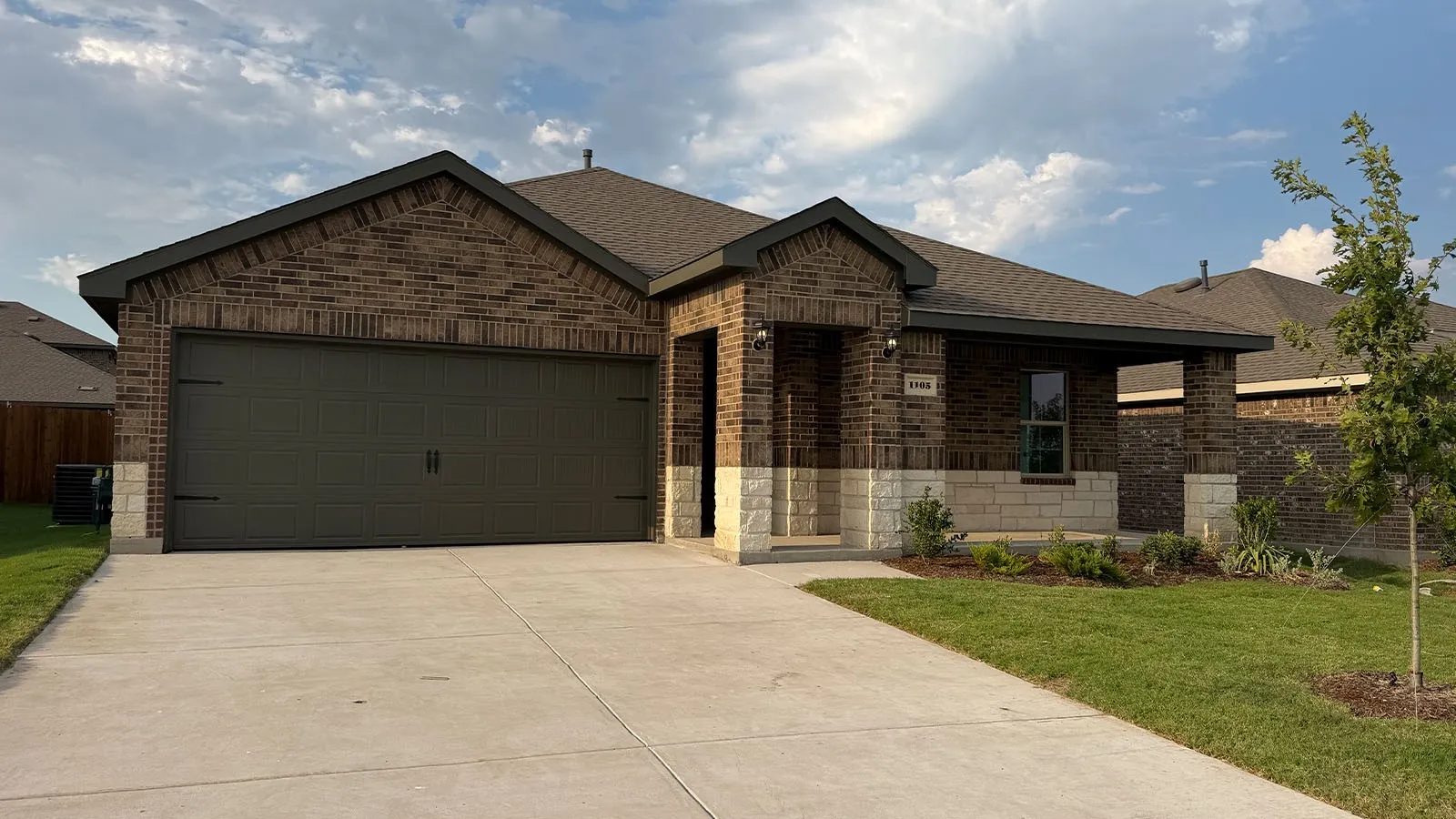 Brick exterior with stone accents, covered entry, attached garage, and manicured landscaping