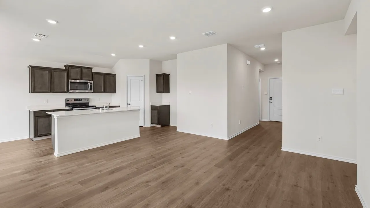 Open-concept living area featuring warm wood-finish flooring throughout, stainless steel appliances, dark cabinetry with white countertops, and recessed ceiling lighting