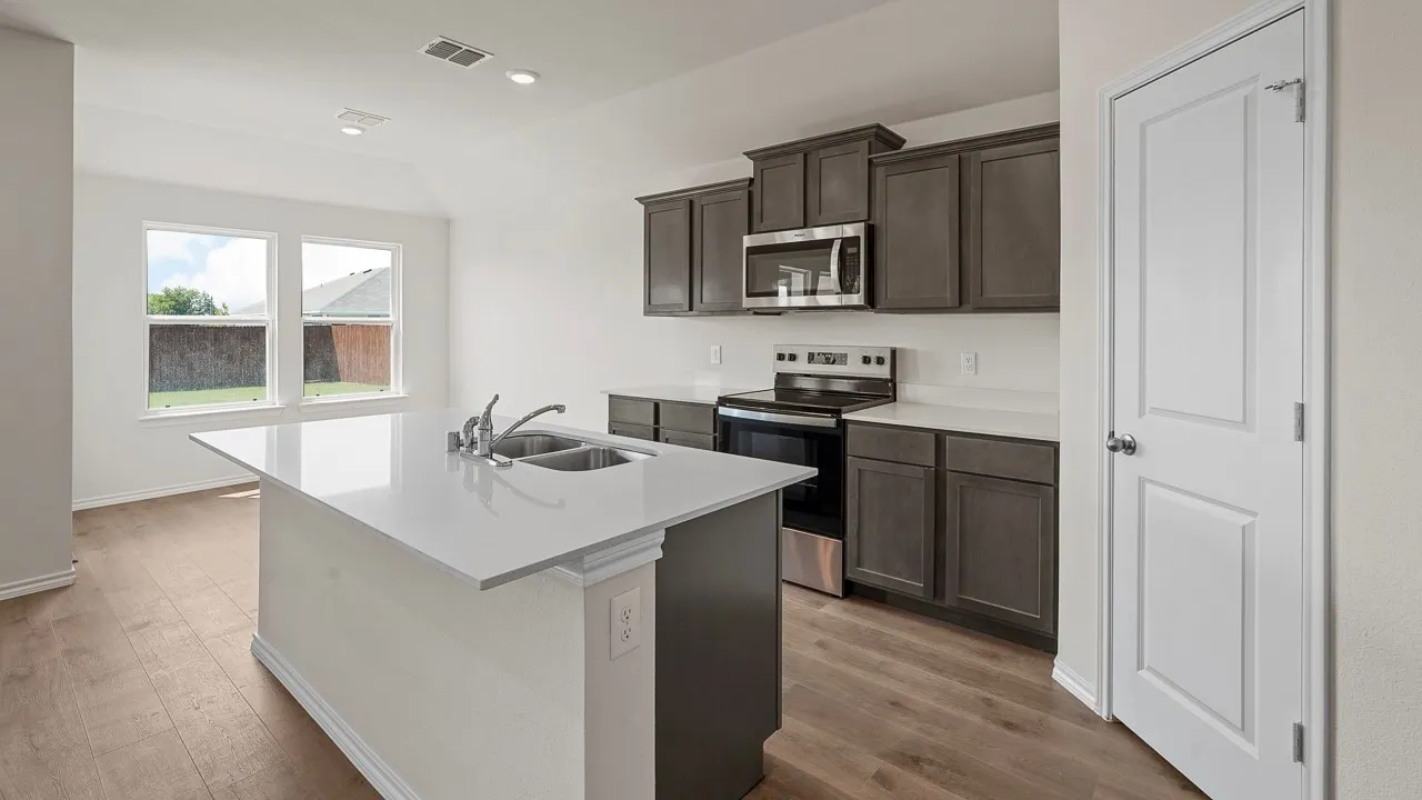 Modern kitchen featuring dark cabinetry with ample storage, white quartz countertops, a center island with seating space, stainless steel appliances, and wood-finish flooring throughout the open-concept layout