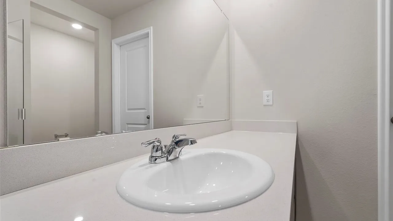 Clean-lined bathroom vanity featuring a round ceramic sink, chrome faucet with dual handles, and a large illuminated mirror