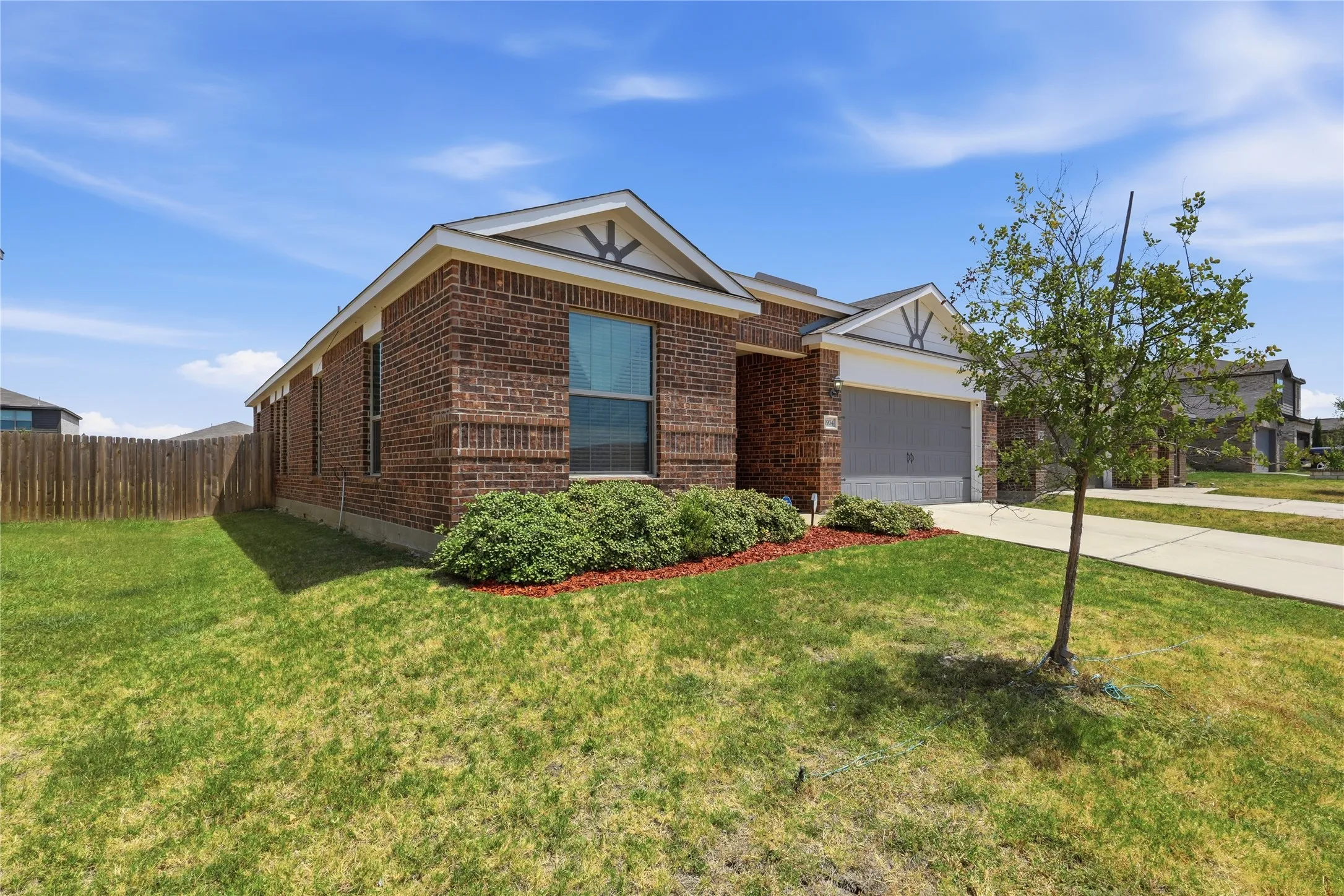 Brick exterior home featuring a gabled roofline with decorative trim, large windows, and an attached garage