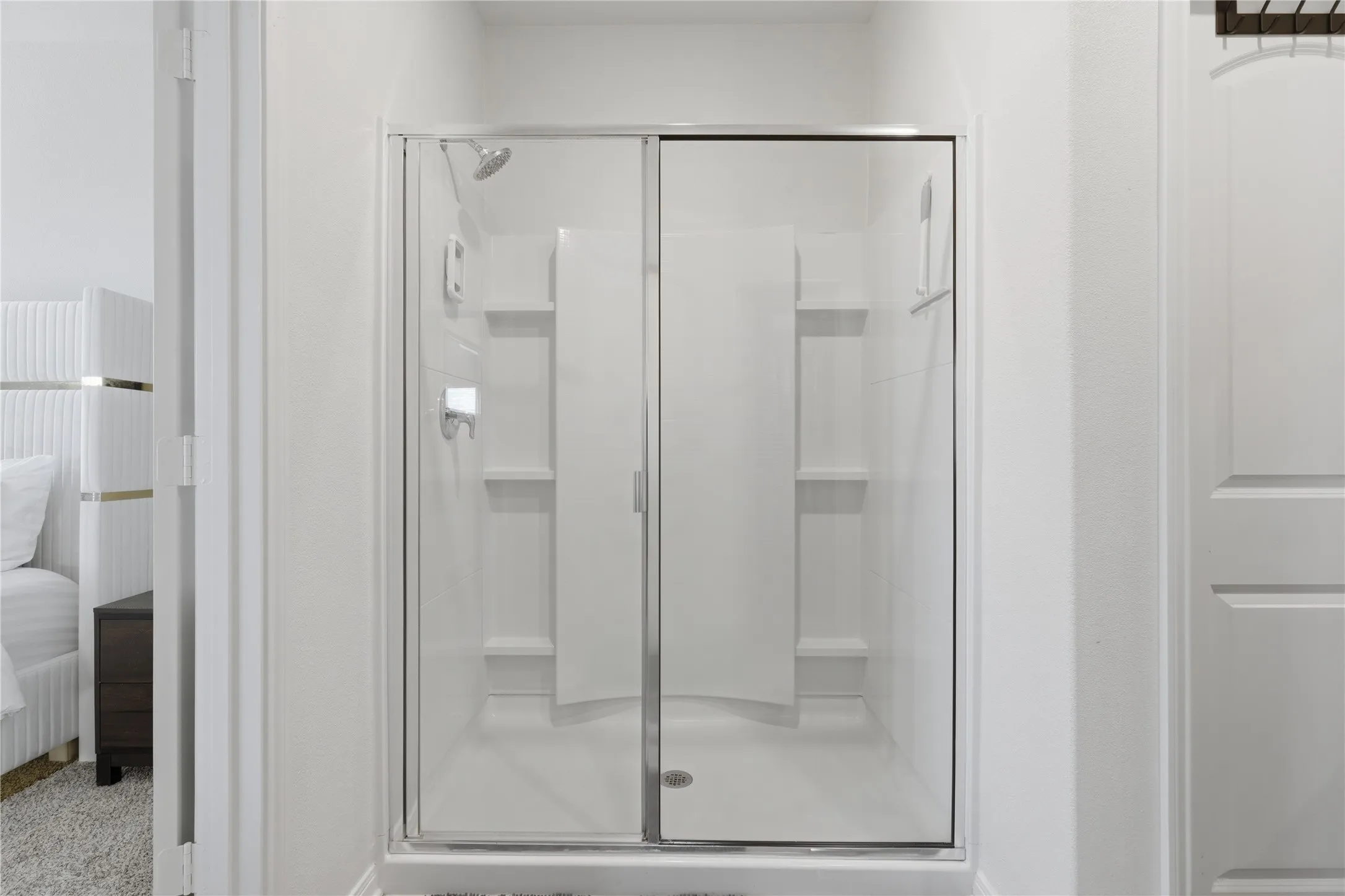 Spa-inspired shower enclosure featuring frameless glass doors, dual showerheads, and integrated shelving throughout the tiled surround for convenient storage and organization
