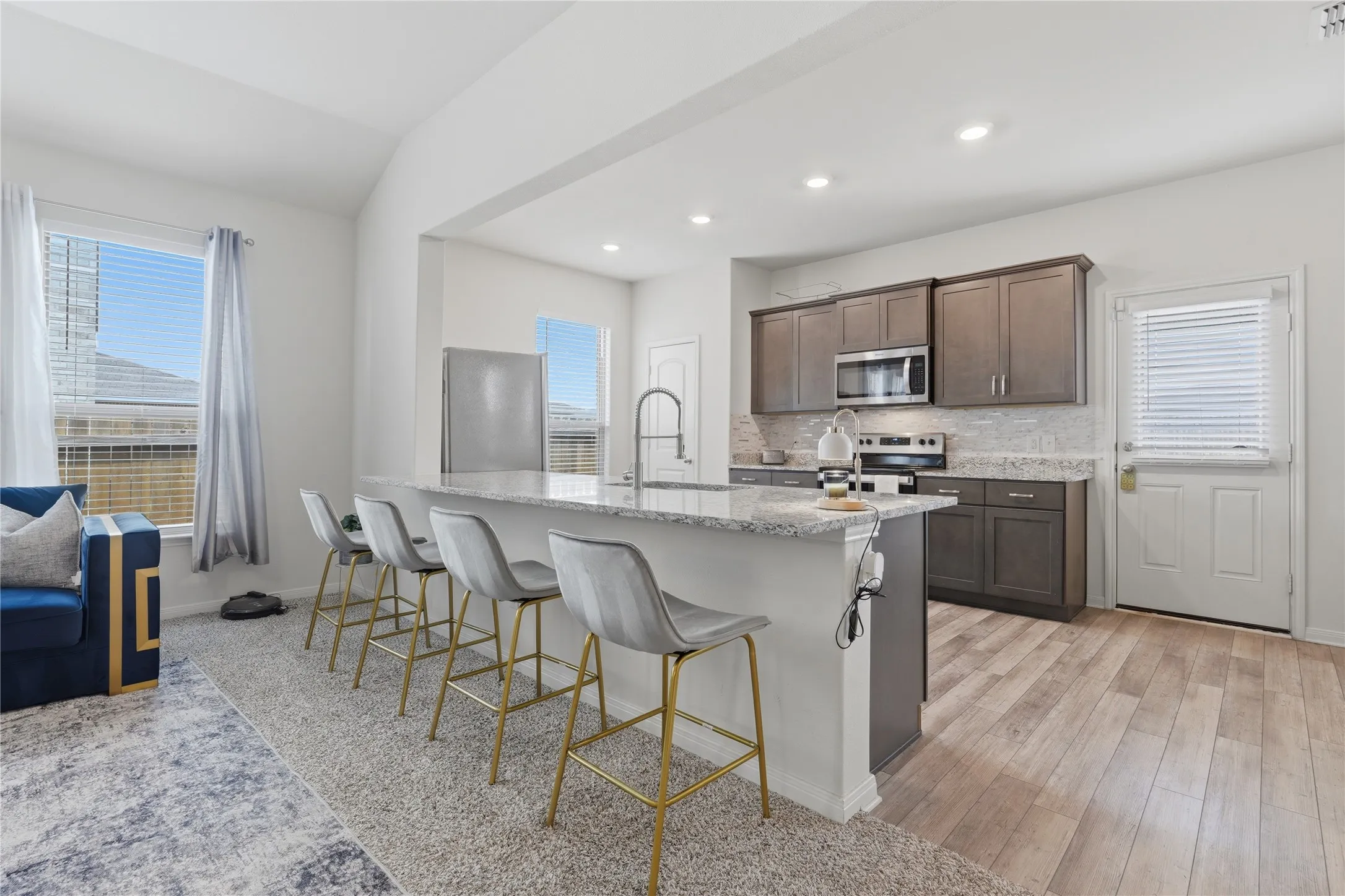 Open-concept kitchen featuring an island with counter seating, stainless steel appliances, dark wood cabinetry, and wood-finish flooring