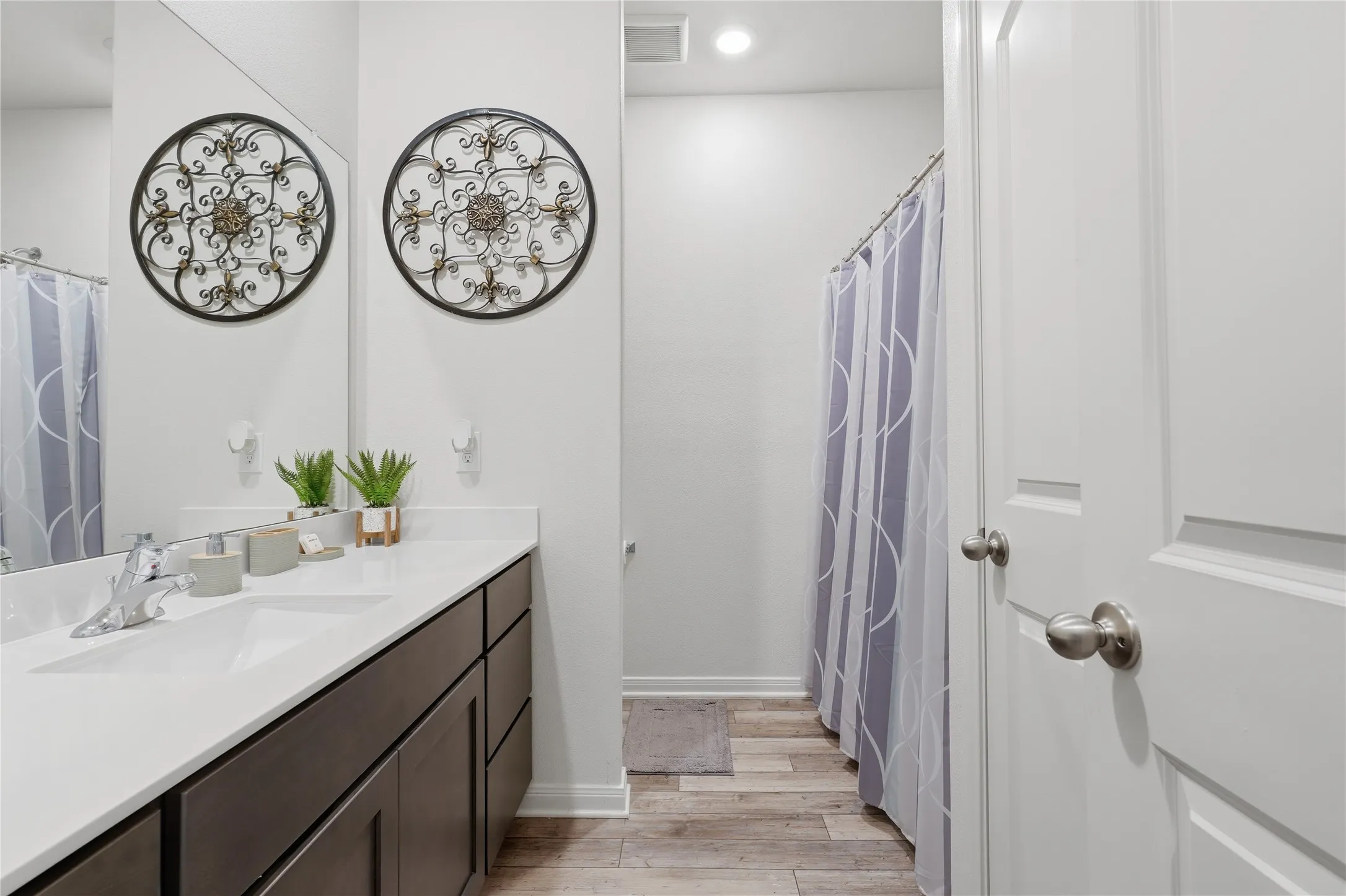 Spa-inspired bathroom featuring dual circular decorative wall sconces, white subway tile surround, wood-finish vanity with white quartz countertop, chrome faucet fixtures, and wood-finish flooring throughout