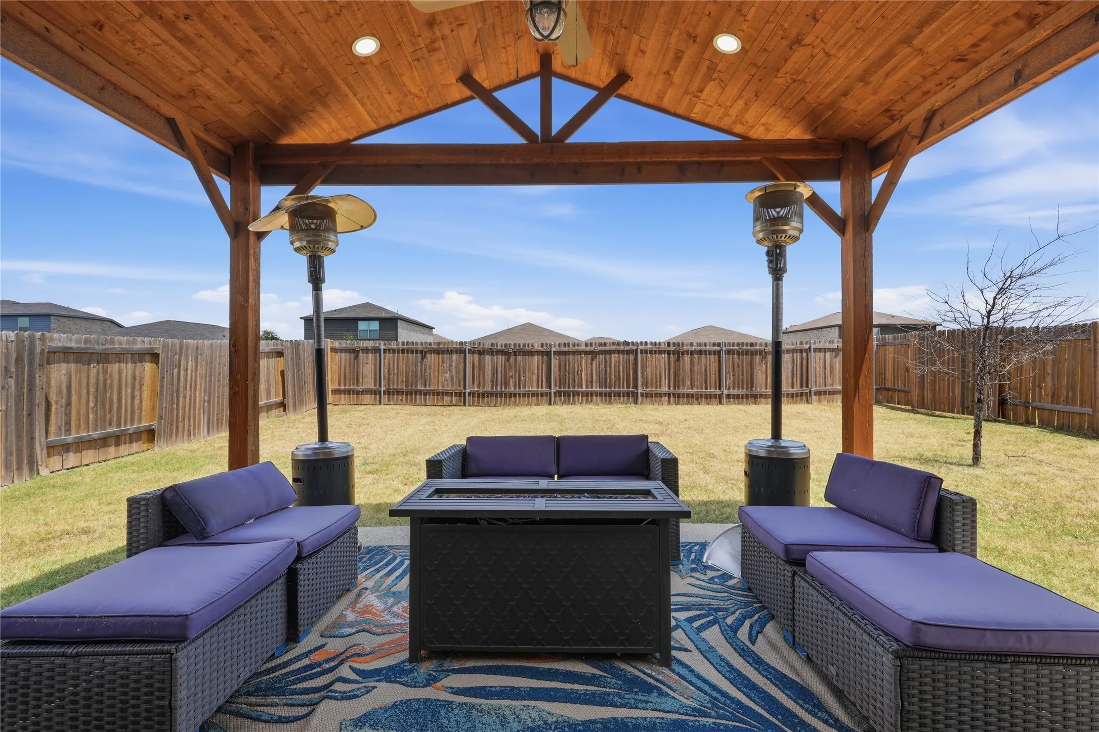 Covered patio with wood-beam construction and gable roof featuring dual infrared heaters, stone fire table, and woven outdoor seating