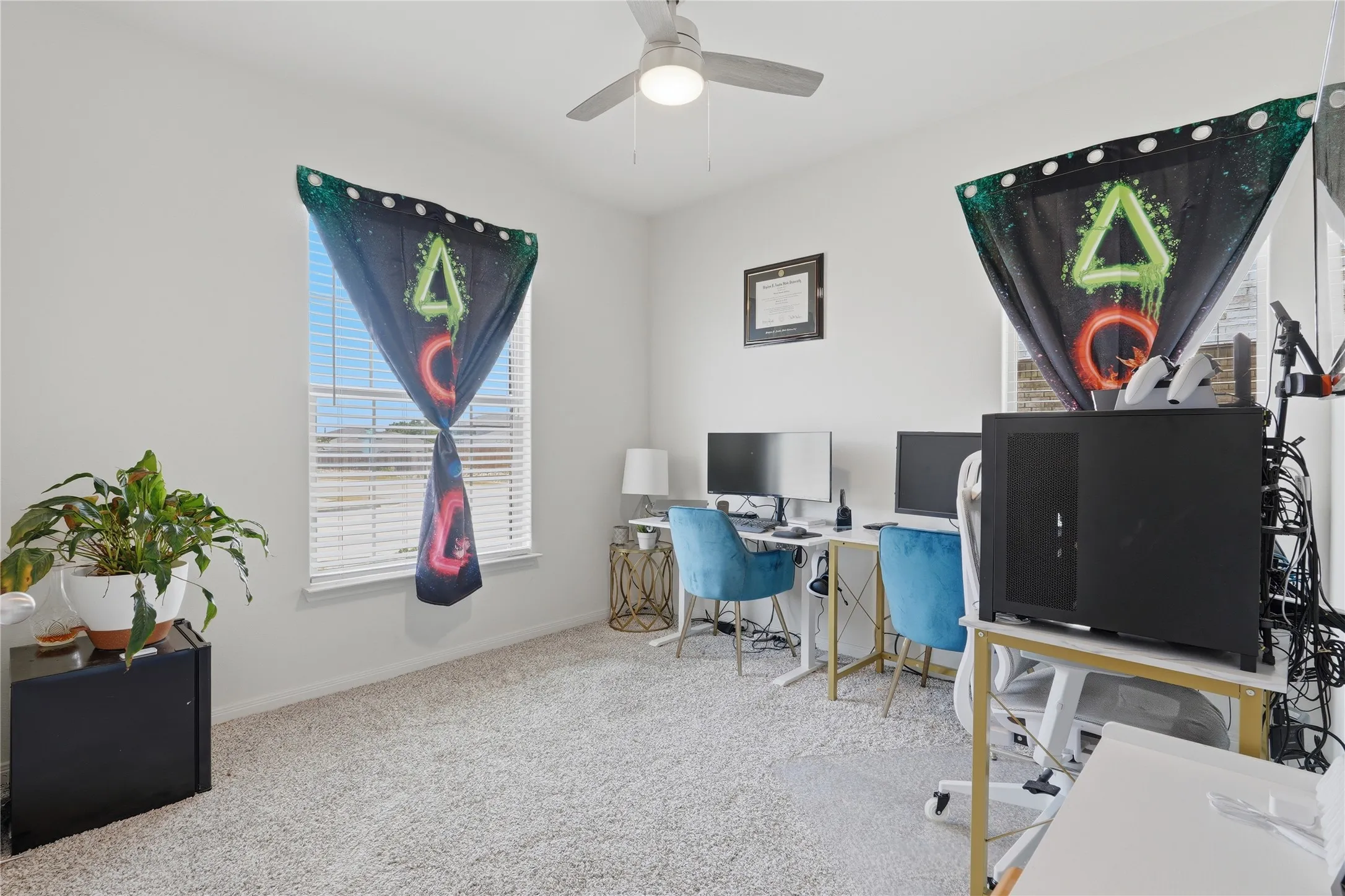 Bright home office featuring carpet flooring, ceiling fan with integrated lighting, and large windows with cellular shades