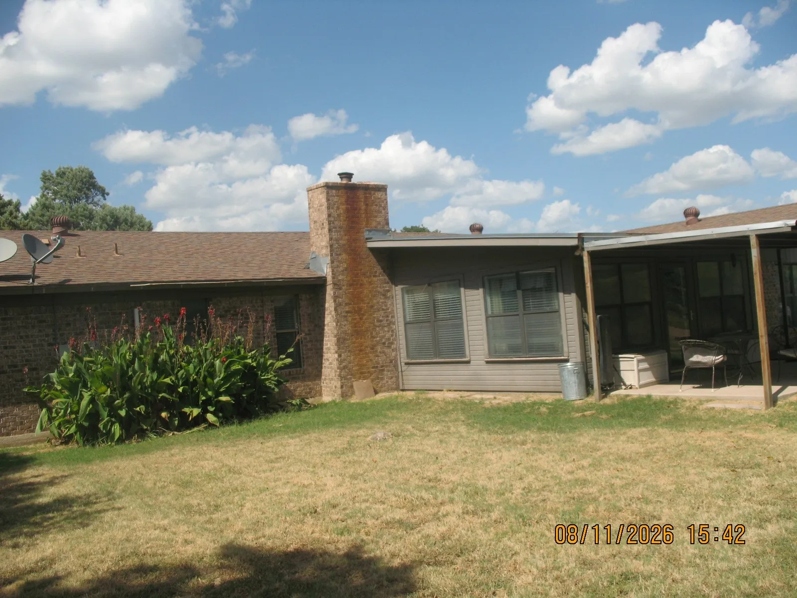 Brick exterior with a prominent brick chimney, shingle roof, and an enclosed patio area