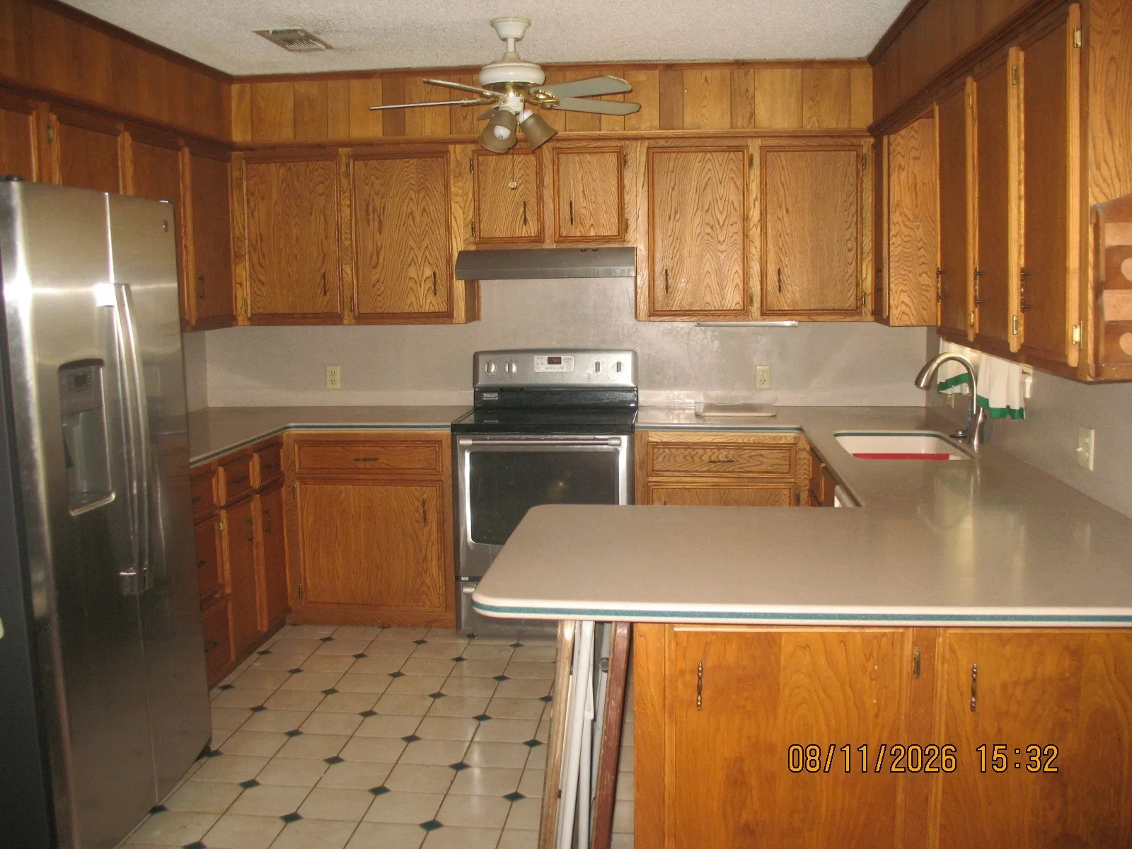 U-shaped kitchen layout featuring wood cabinetry, light-toned countertops, tile flooring, and a stainless steel appliance suite