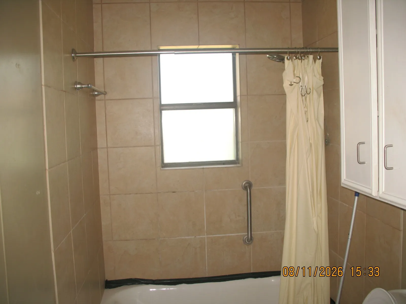 Tiled bath enclosure with a window, tub, and grab bar