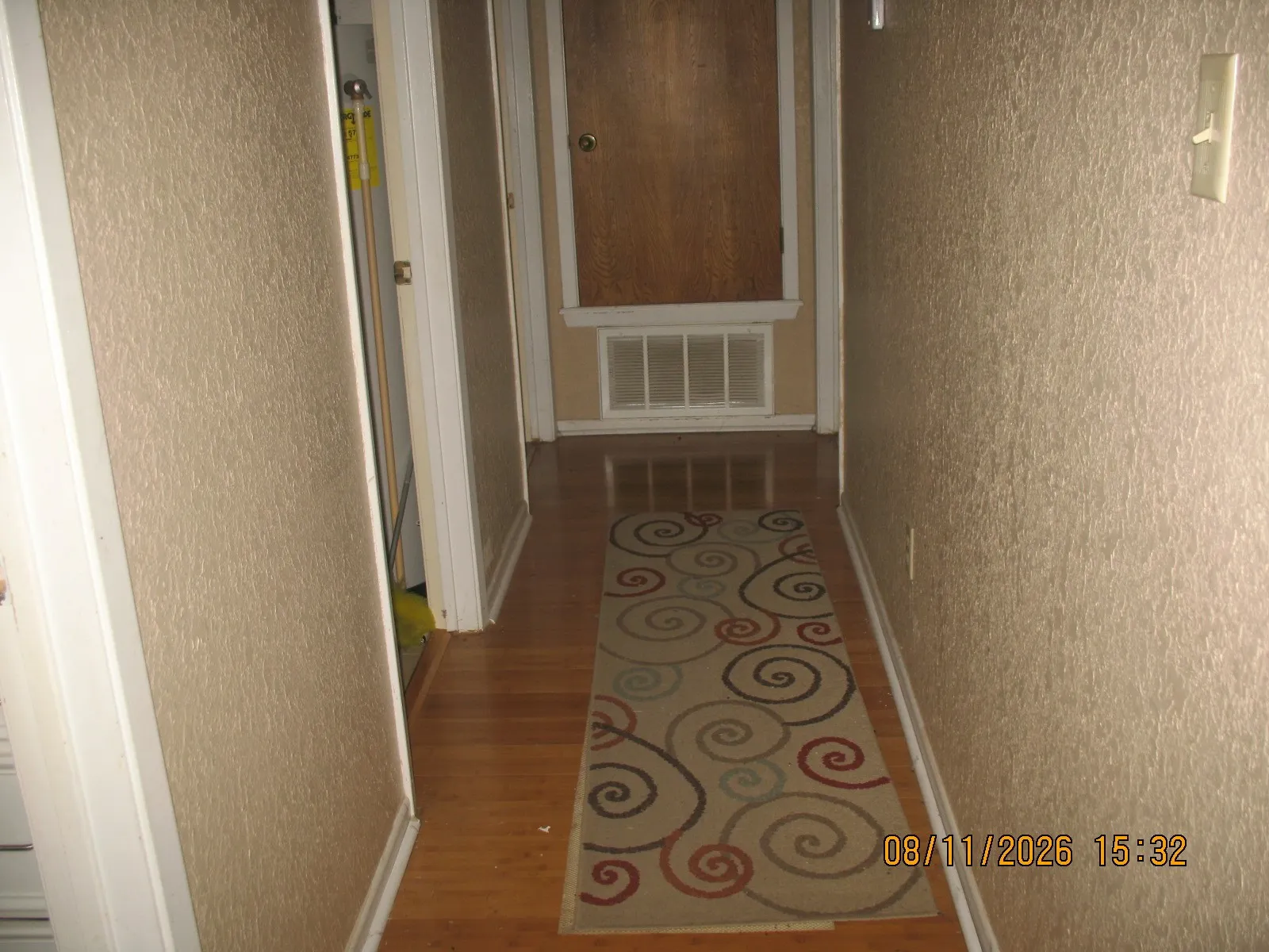 Wood-finish flooring with white trim, textured wall finishes, and a wall-mounted light switch