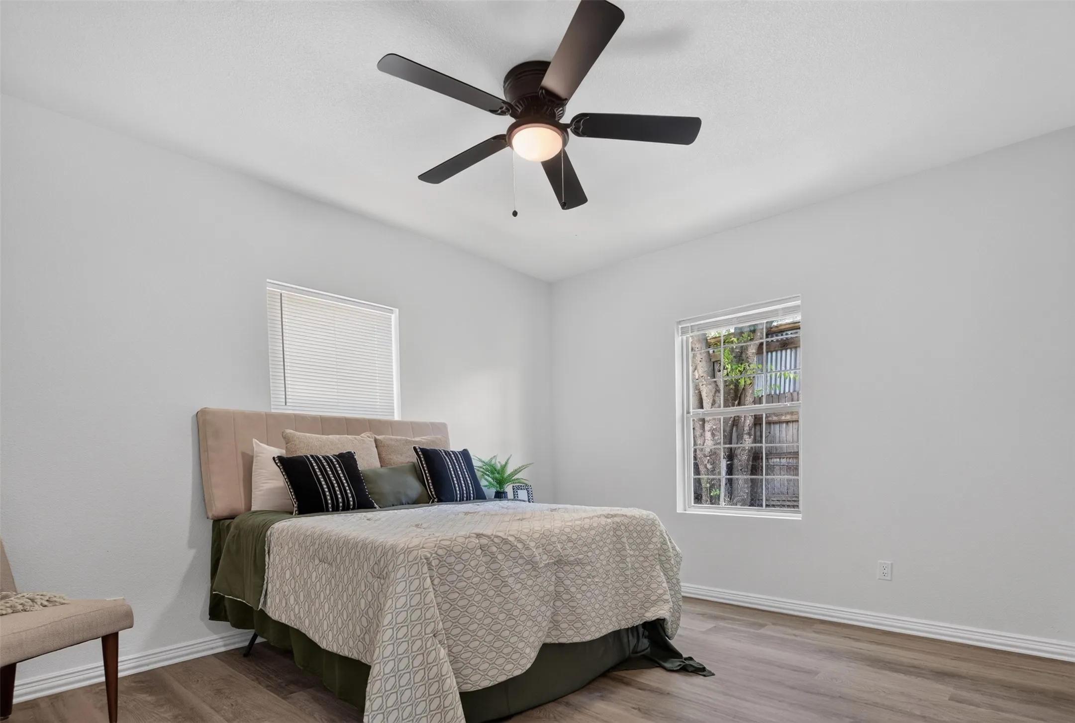 Bright secondary bedroom with wood-finish flooring, dual windows providing natural light, and a contemporary ceiling fan with integrated lighting fixture